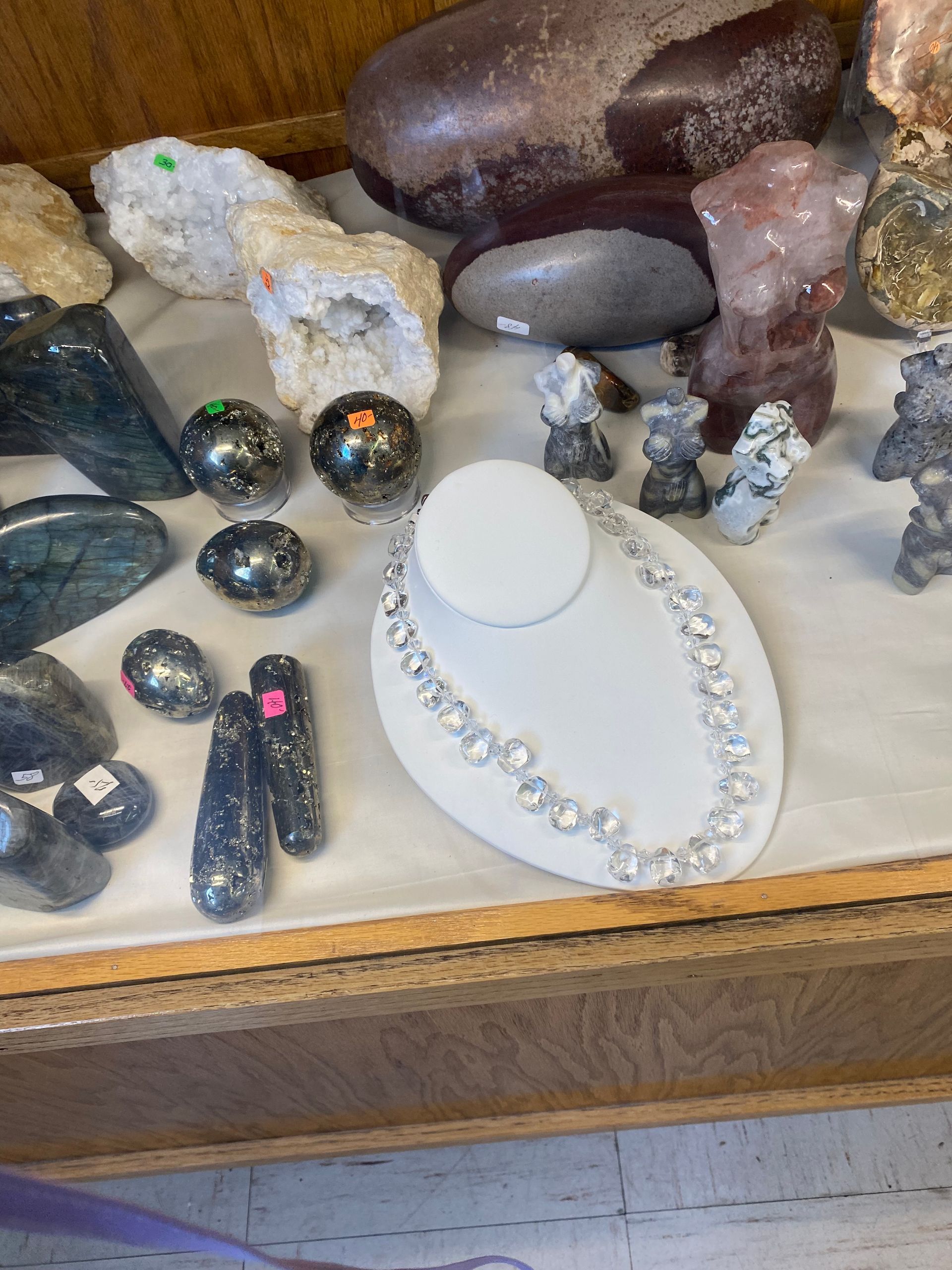 Assorted jewelry and polished stones displayed on a shelf with a white necklace bust.
