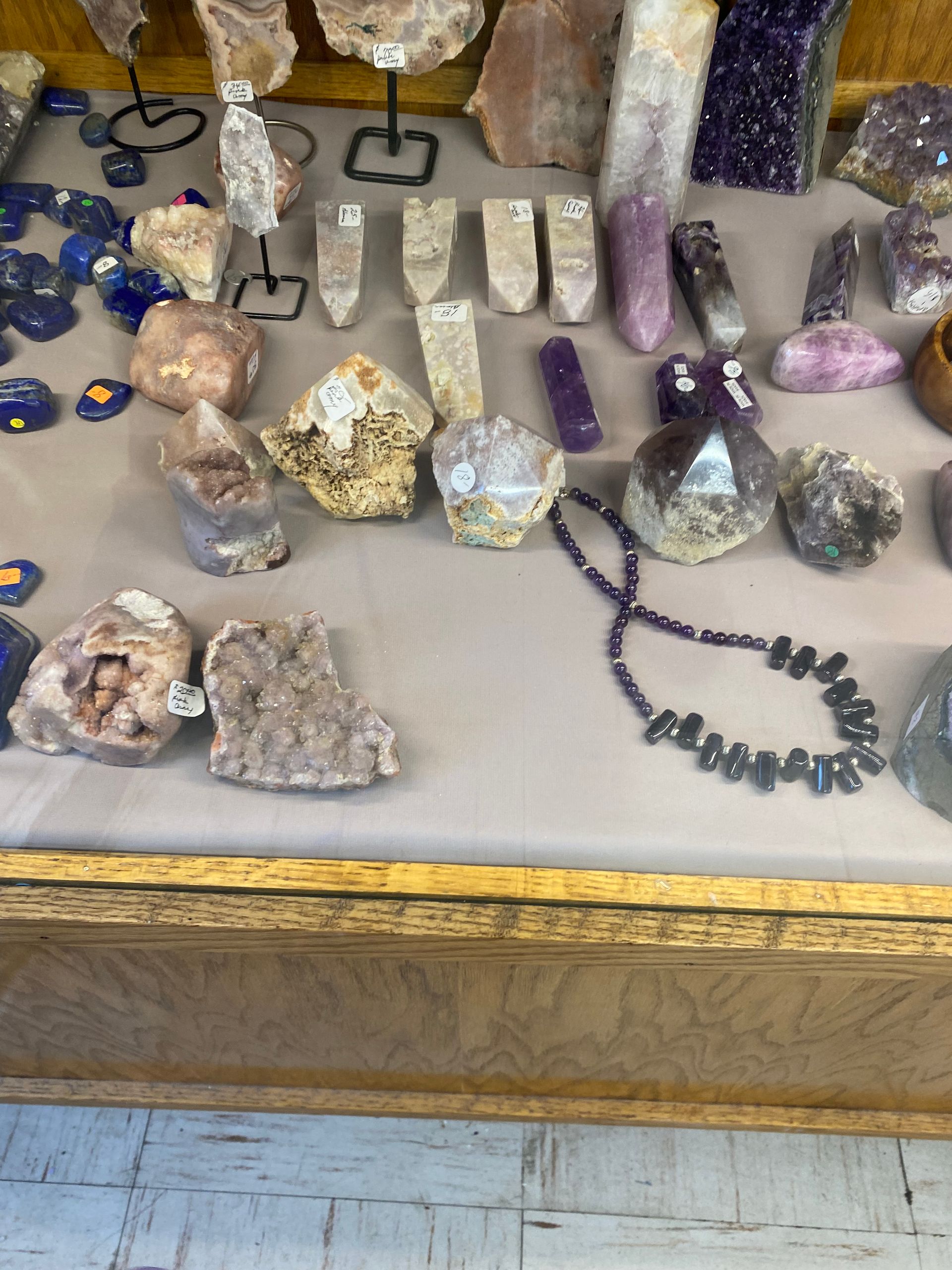 Display of assorted crystal and mineral specimens on a table, including purple amethyst and polished stones.