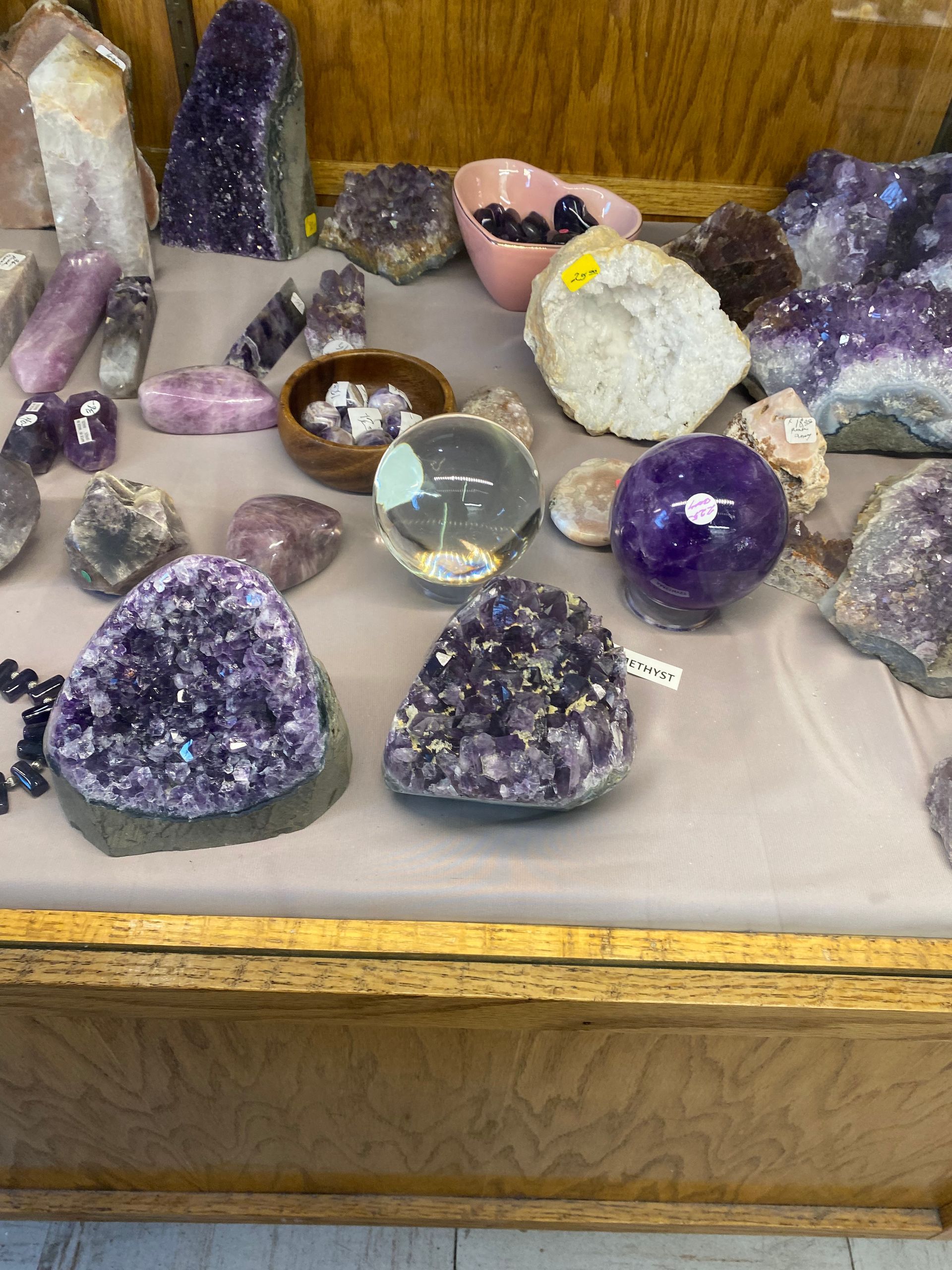 Assorted amethyst and crystal mineral display on a wooden shelf, including purple geodes and polished stones