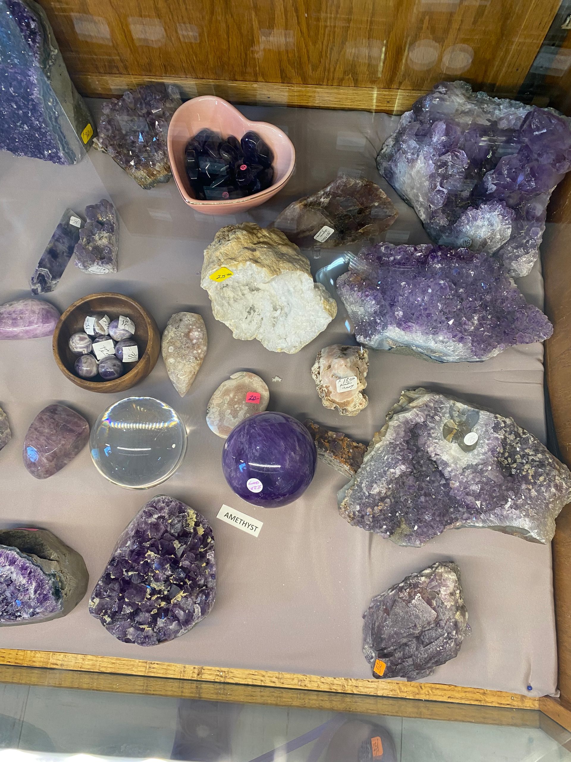 Assorted polished crystals and geodes displayed in a wooden tray, including purple amethyst clusters and quartz pieces