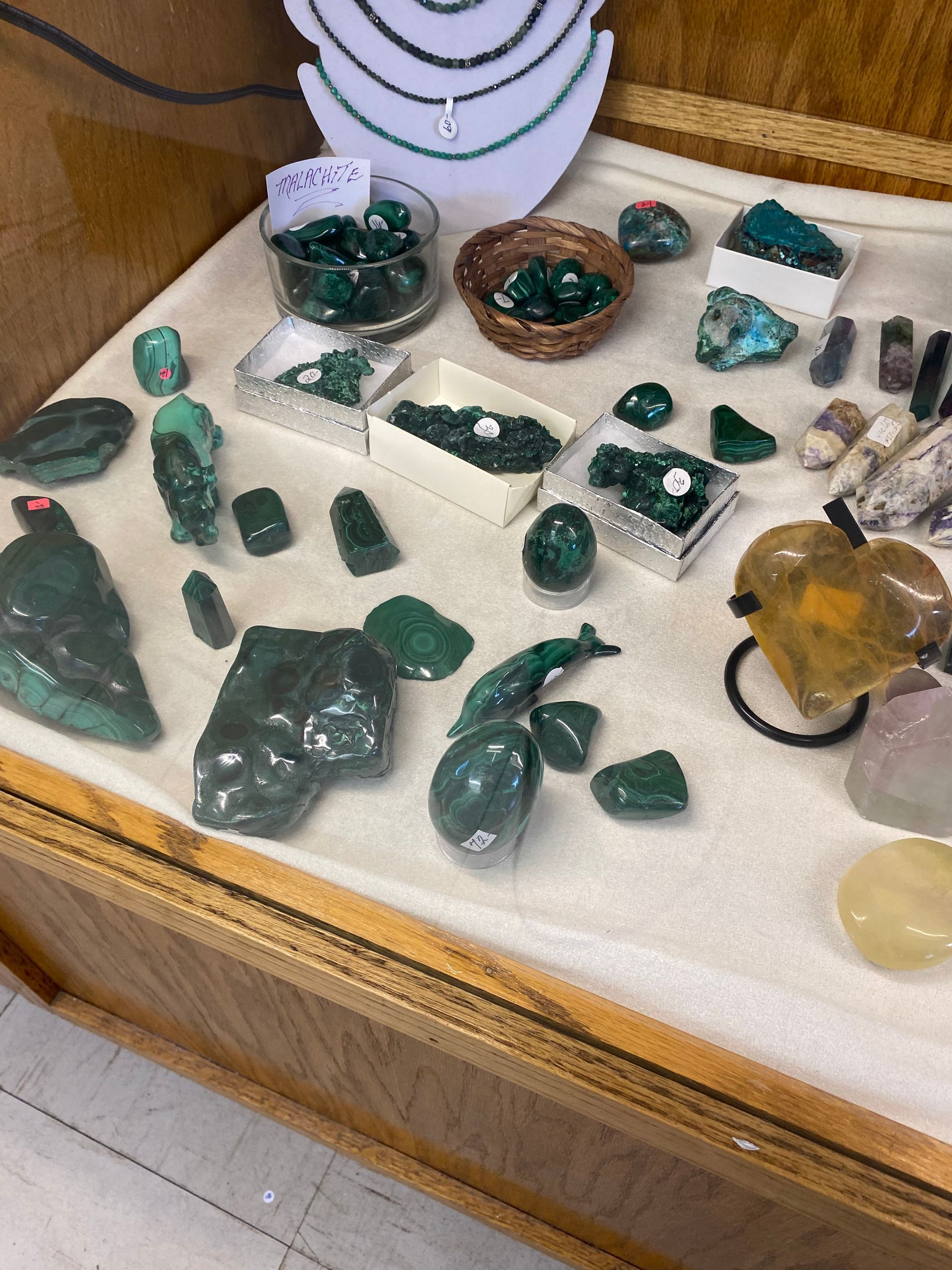 Display case of green gemstones and crystals, with one large amber stone in the front right