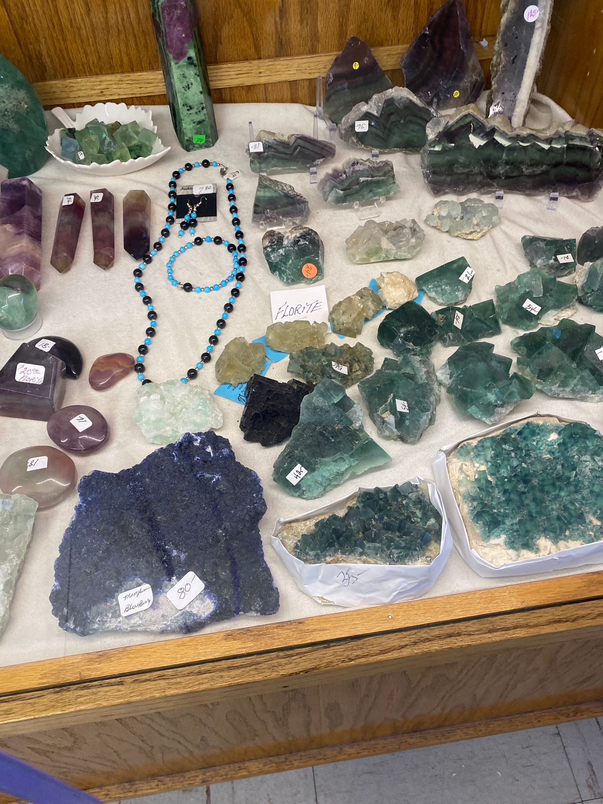 Assorted crystals and gemstones displayed in a wooden tray, including green, clear, purple, and blue pieces.