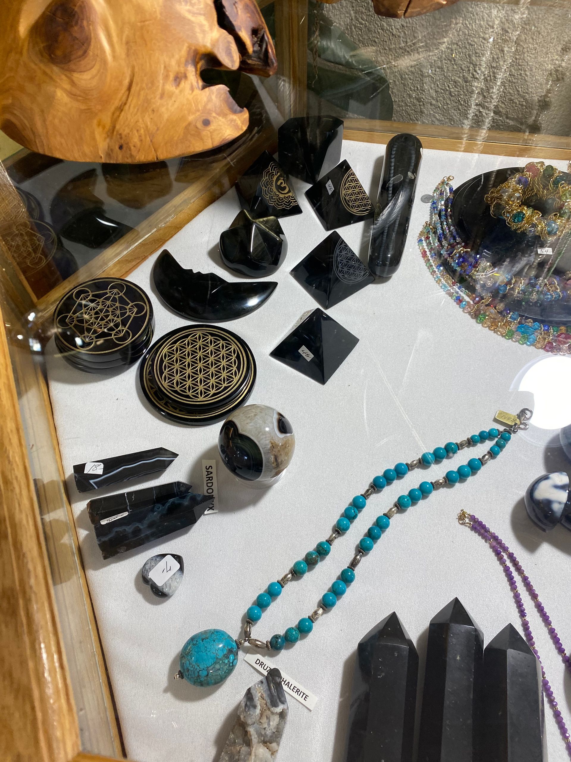 Display case of black stone carvings and turquoise-beaded jewelry on glass with a wood sculpture fragment
