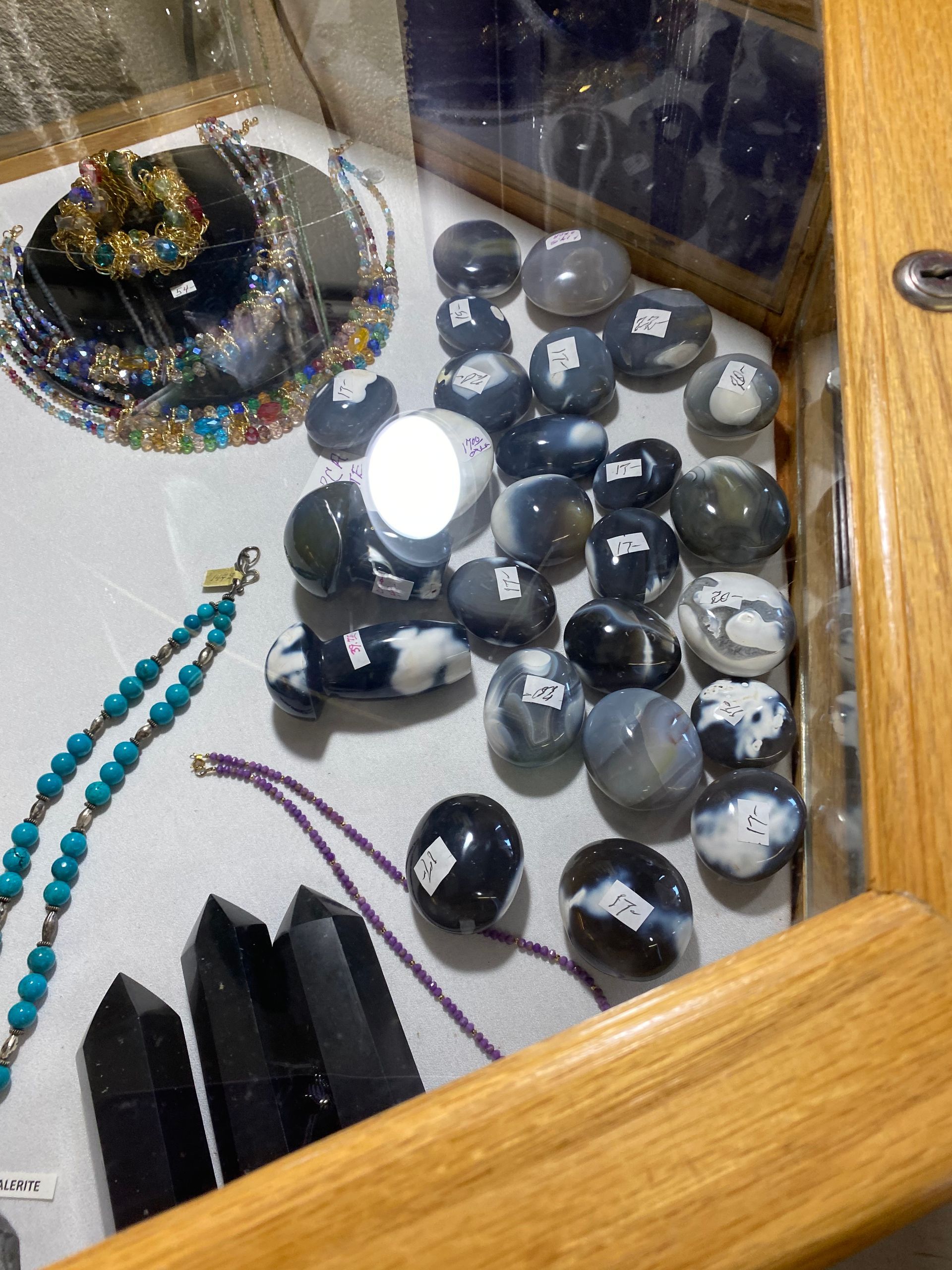 Assorted beaded necklaces and black crystal-like objects displayed in a glass case