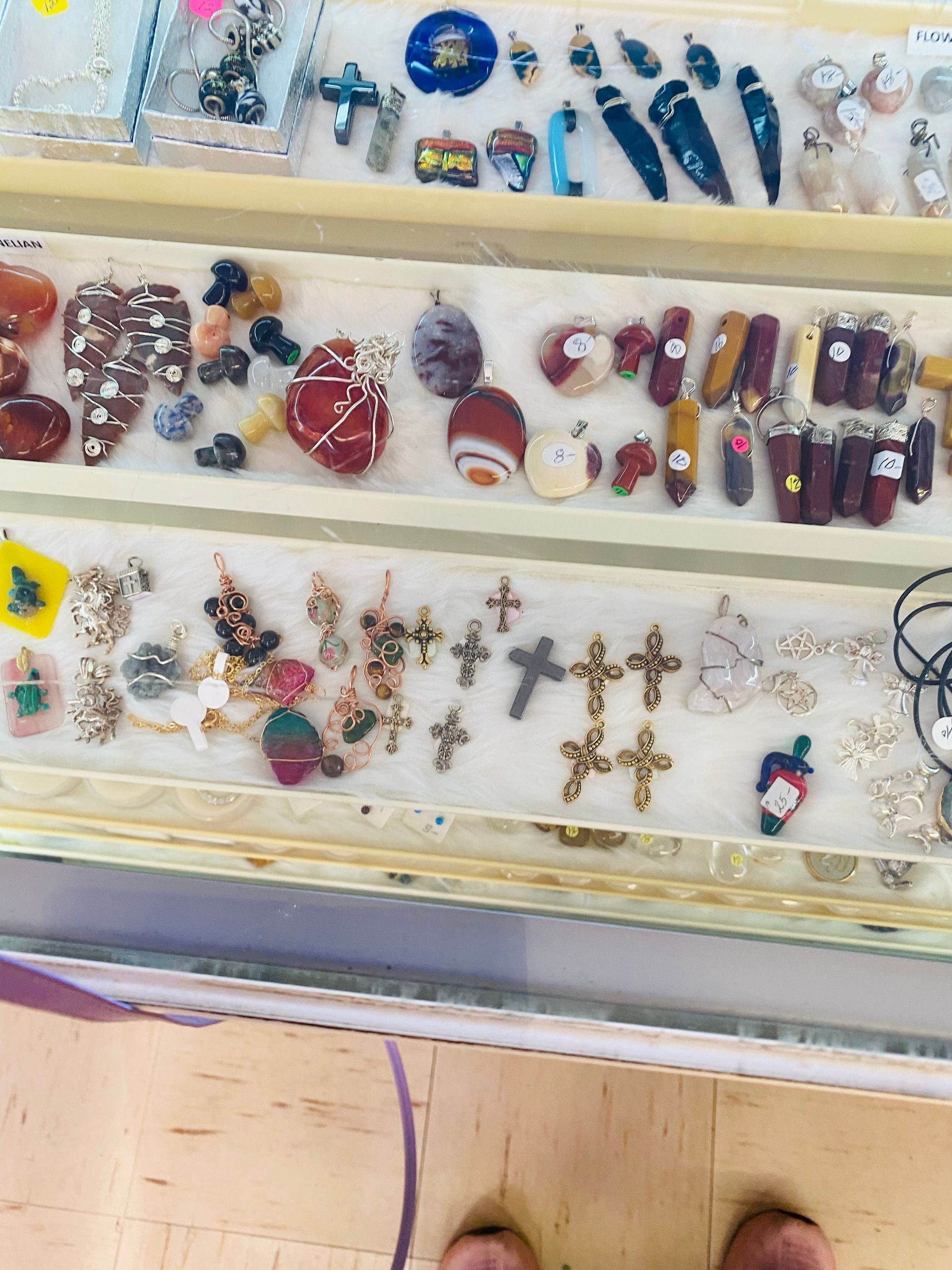 Display case of assorted colorful jewelry, including rings, earrings, necklaces, and crosses, on white trays.