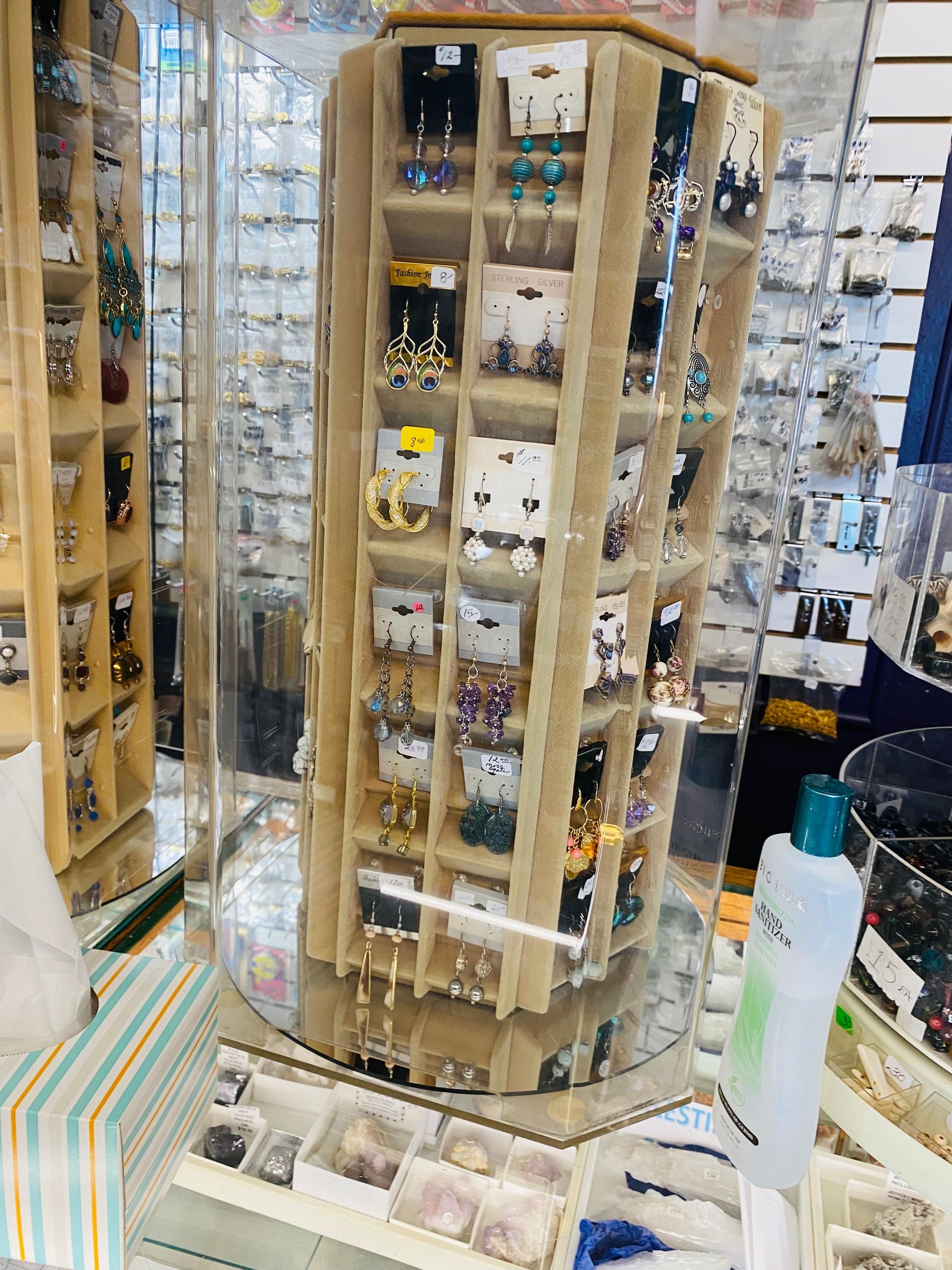 Tall display tower of small perfume or cosmetic bottles in a shop, with samples and a counter below.