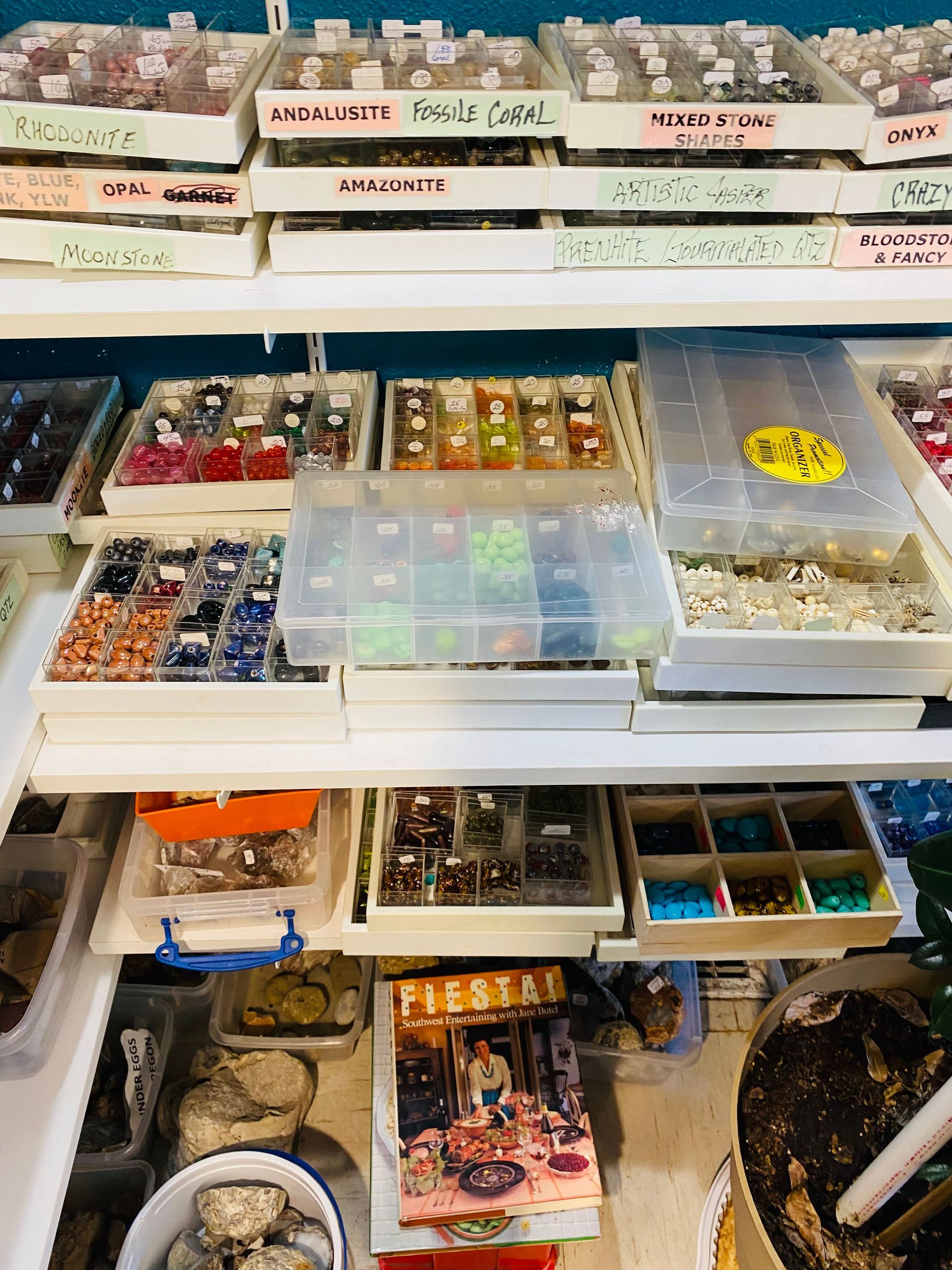 Display of assorted beads and craft supplies in labeled plastic containers and trays.