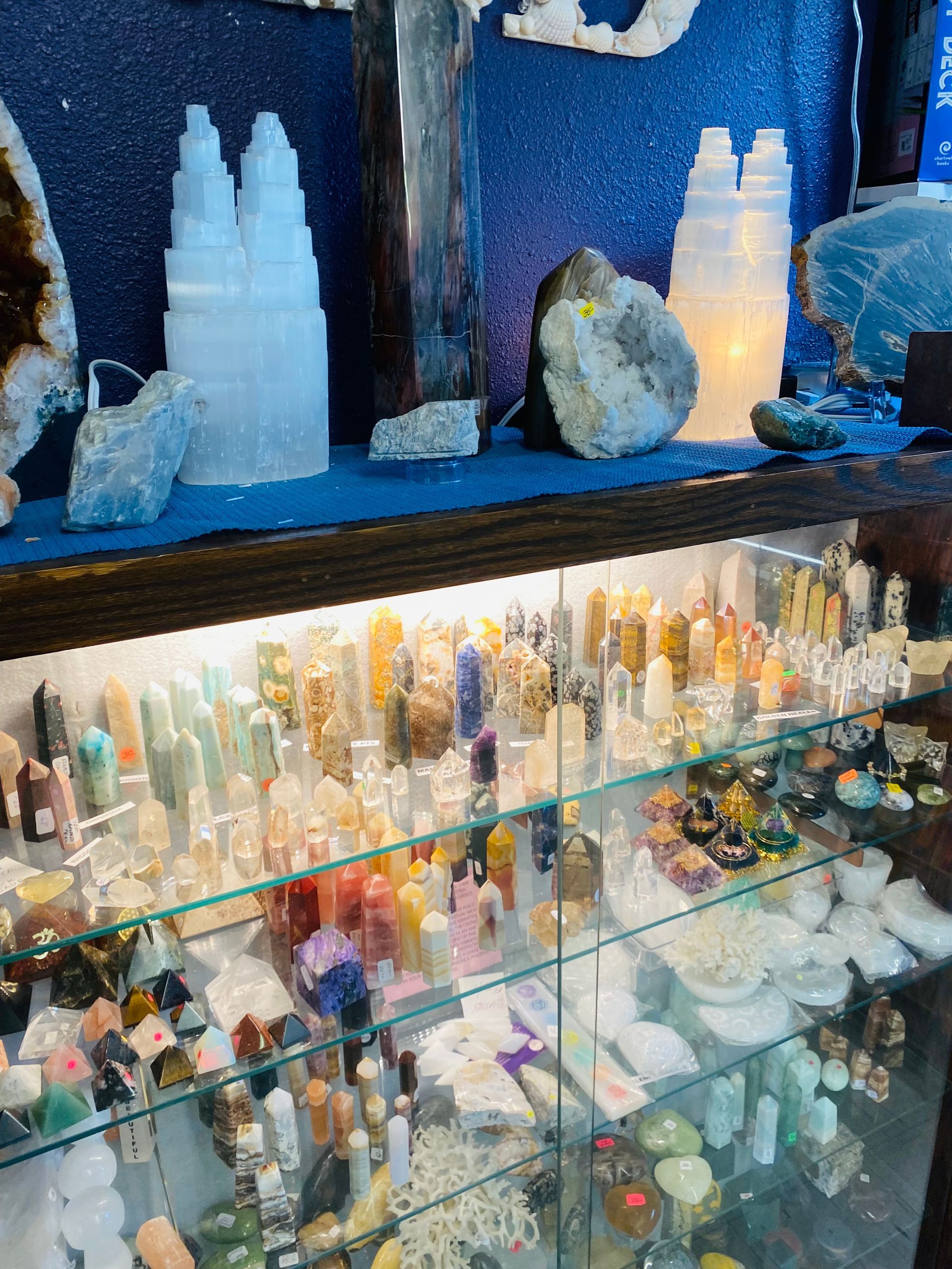 Blue-lit crystal and mineral display with assorted gemstones on shelves and in glass cases