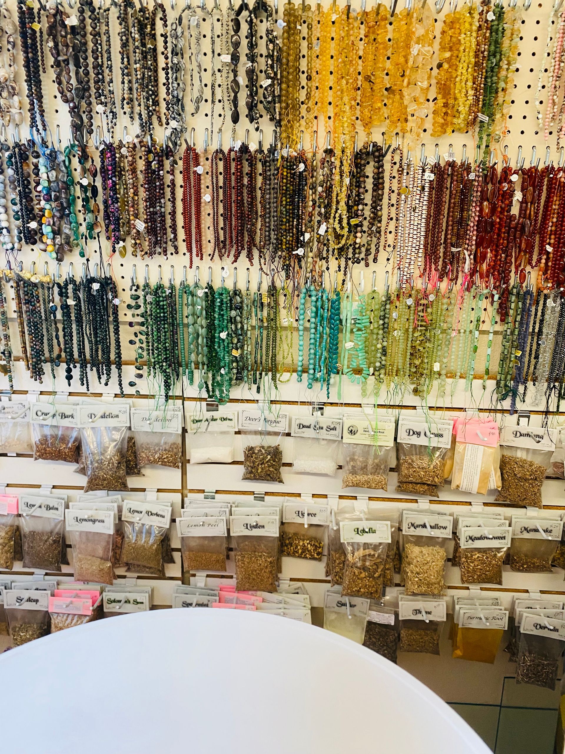 Display of beaded jewelry and small labeled bins in a shop, with a white chair in front