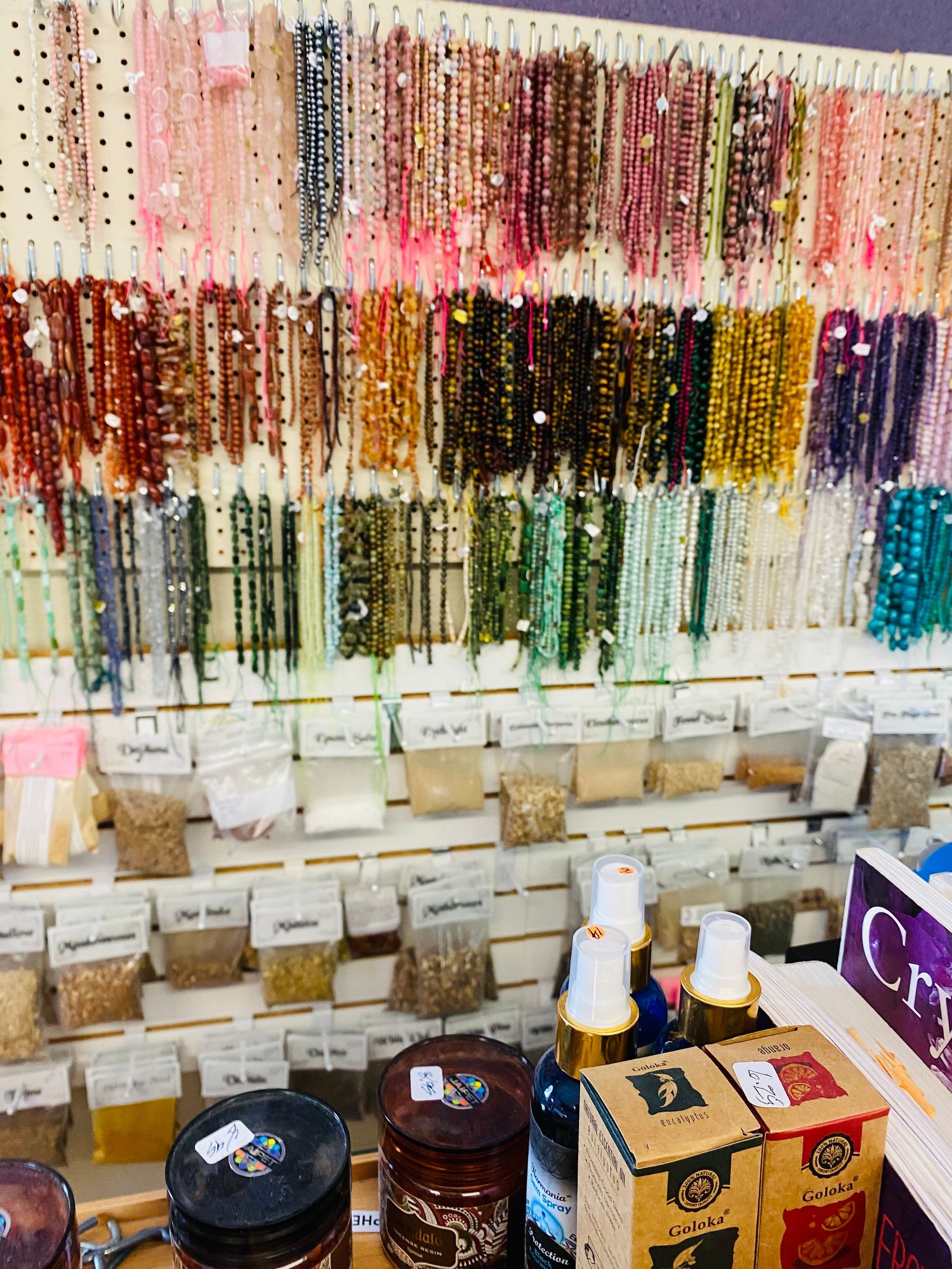 Wall of colorful hanging beaded necklaces above a shelf of candles and small gift items in a shop