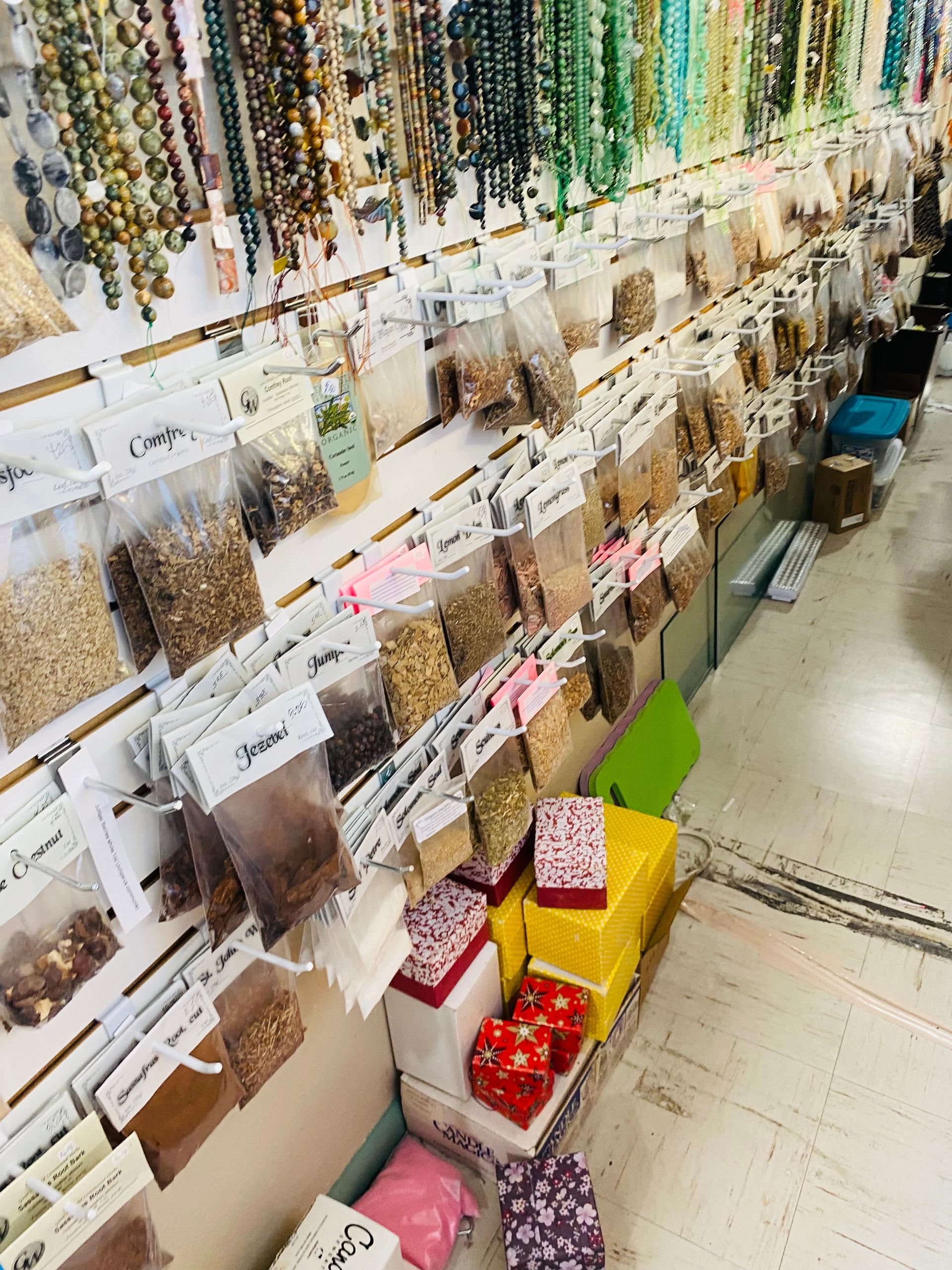 Rows of hanging craft supplies and beads in a shop aisle, with colorful boxes on the floor.