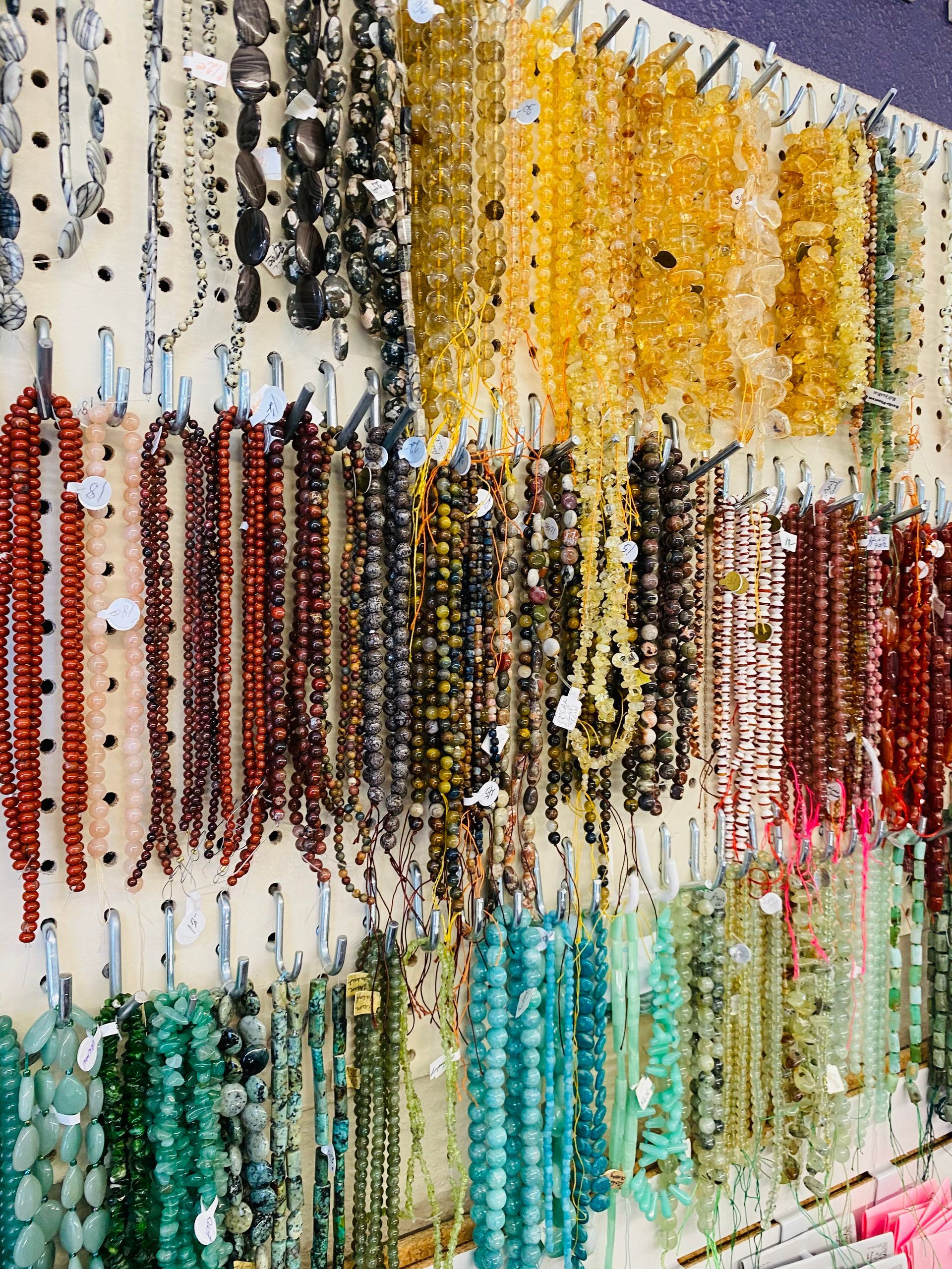 Rows of colorful hanging bead strands in a craft display, with yellow, red, teal, green, and white beads