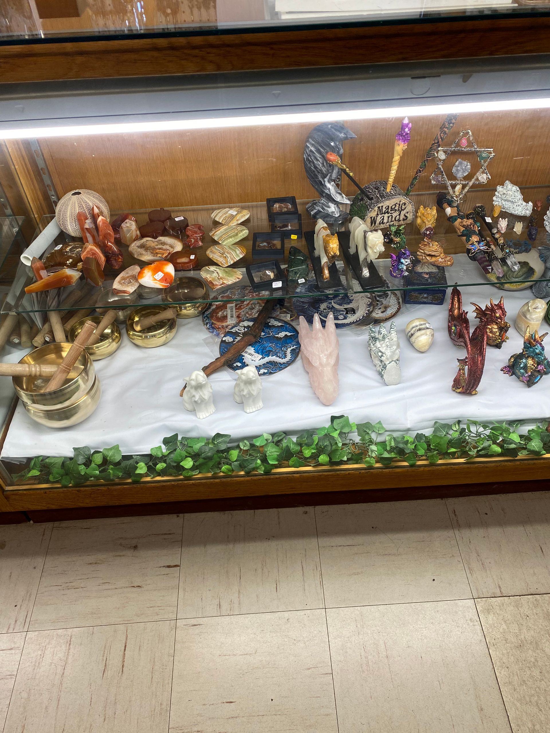 Decorative display with small figurines and ornaments on a white cloth-covered table under glass.