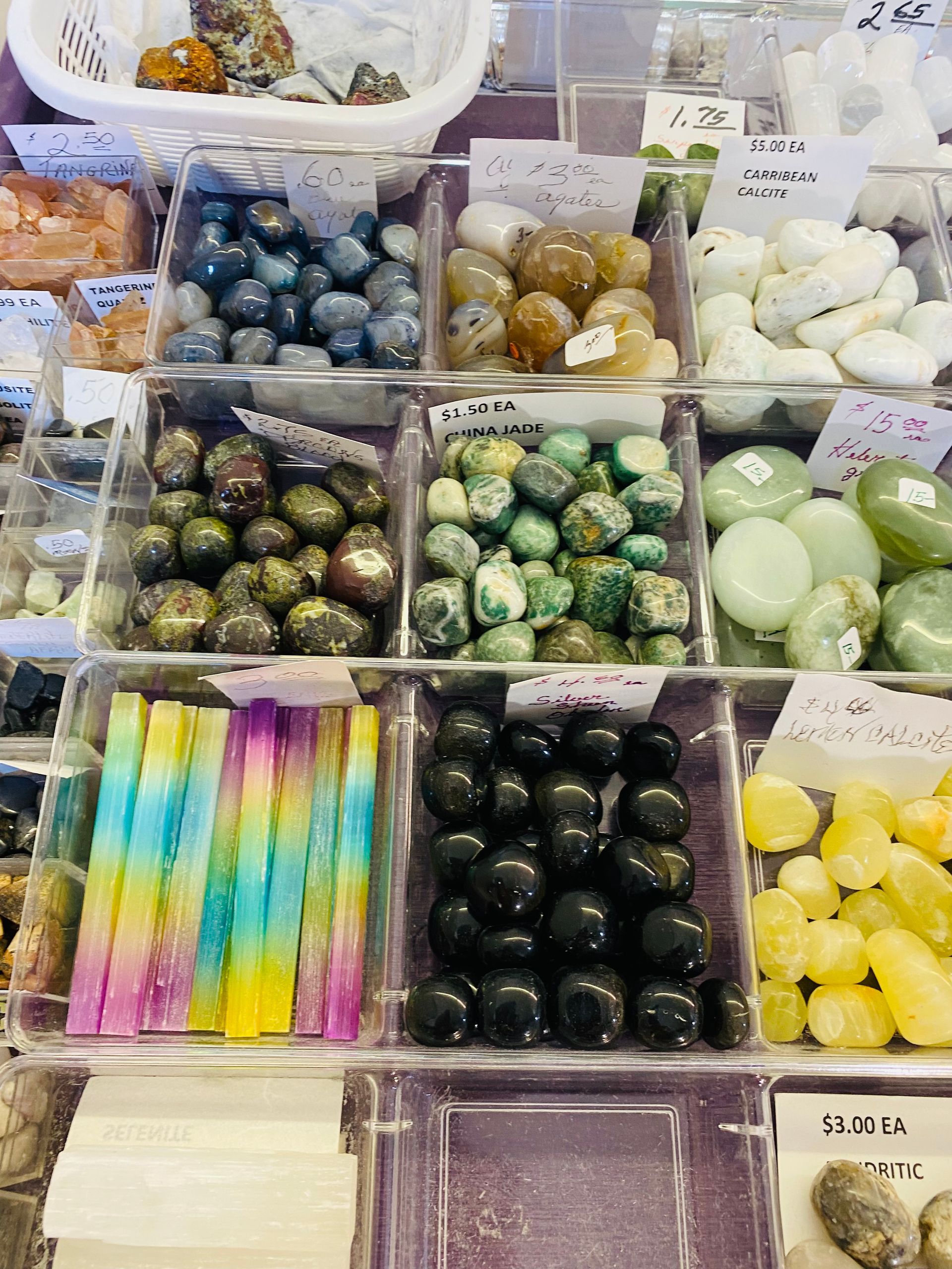 Assorted colorful crystal stones and mineral beads displayed in small bins at a market stall