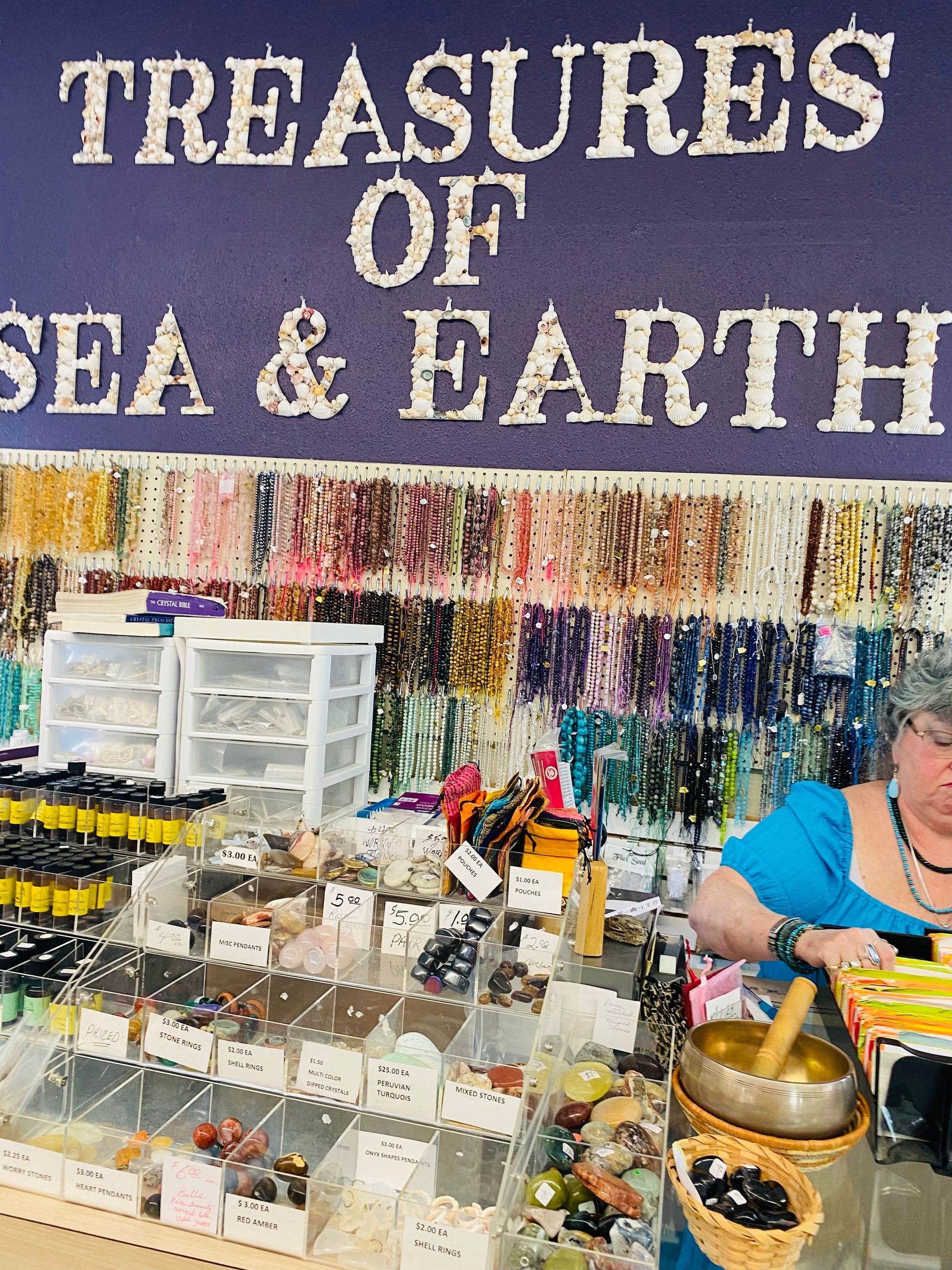 Market stall with “Treasures of Sea & Earth” sign, displaying jars, trinkets, and colorful goods