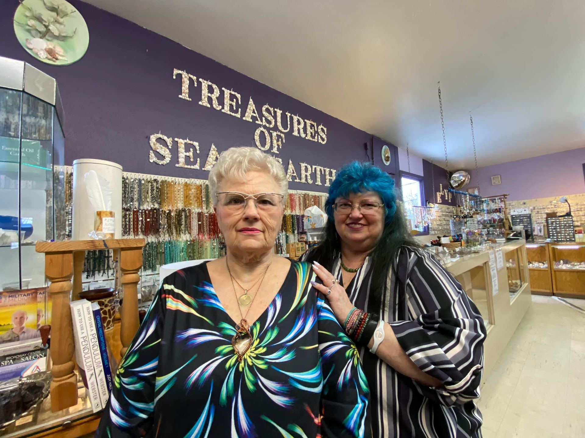 Two people posing in a shop, one in a black-and-blue dress, one in striped shirt and blue hat