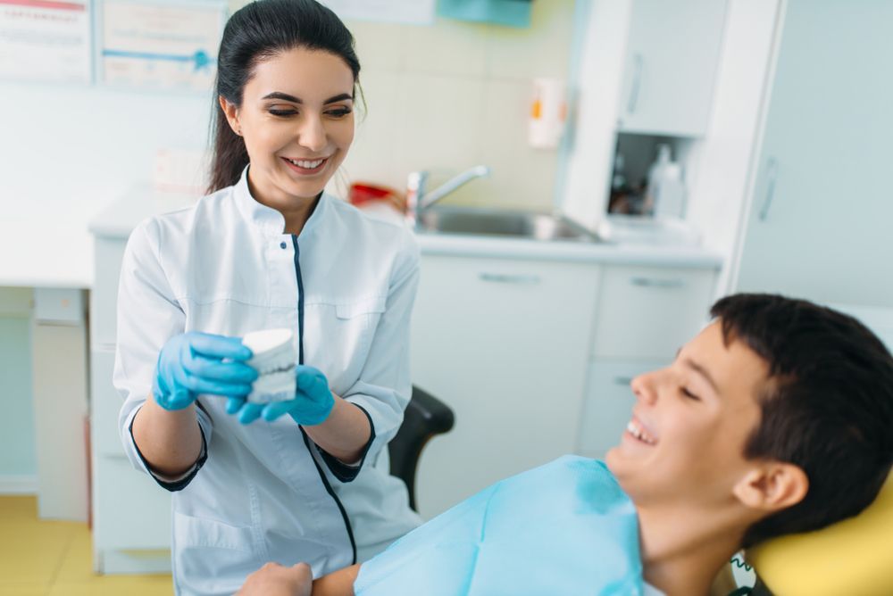 Dentist showing a tooth model to a patient in a dental office, both smiling.
