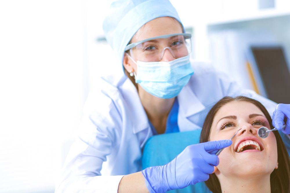 Dentist in blue scrubs and mask examining a patient's teeth with tools.