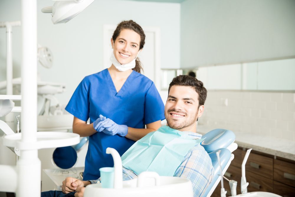 Dentist and patient smiling in a dental office. The dentist is wearing blue scrubs.