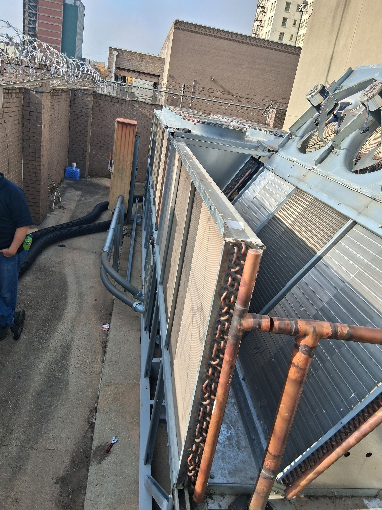 Rooftop HVAC units beside a brick wall, with copper pipes and a person crouching at left