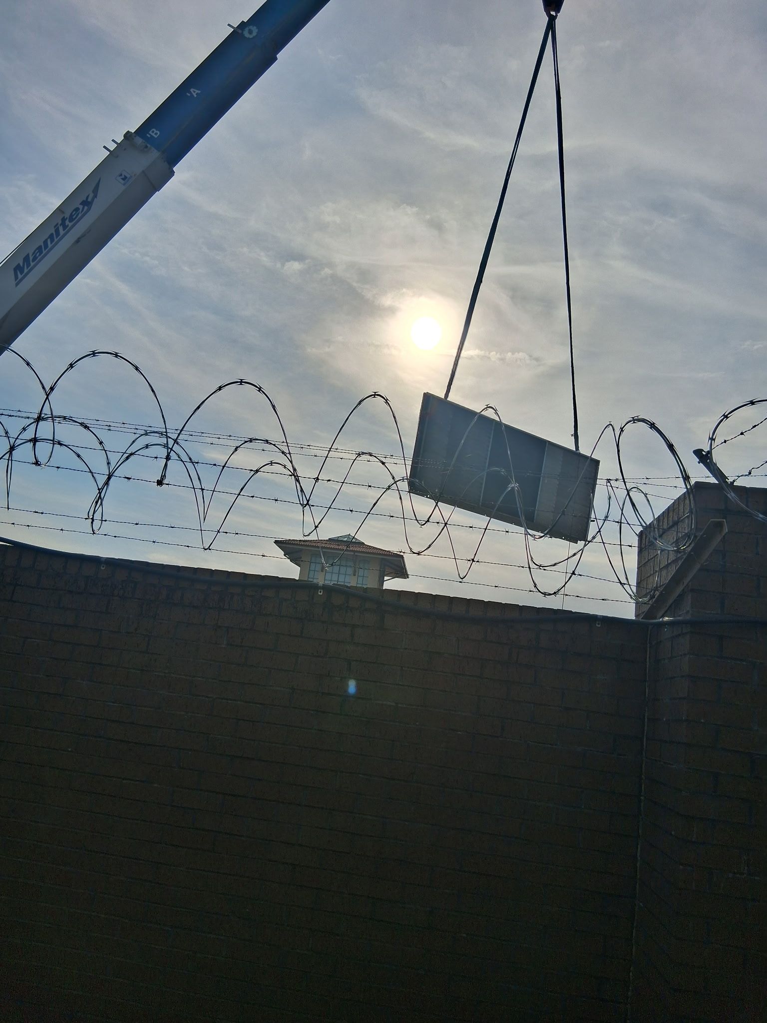 Crane lifting a container over a barbed-wire fence at sunset