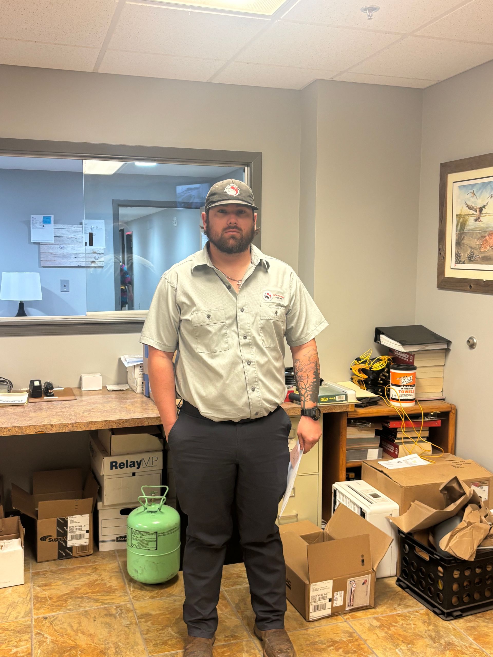 Man standing in an office beside stacked boxes and a green propane tank, facing the camera.
