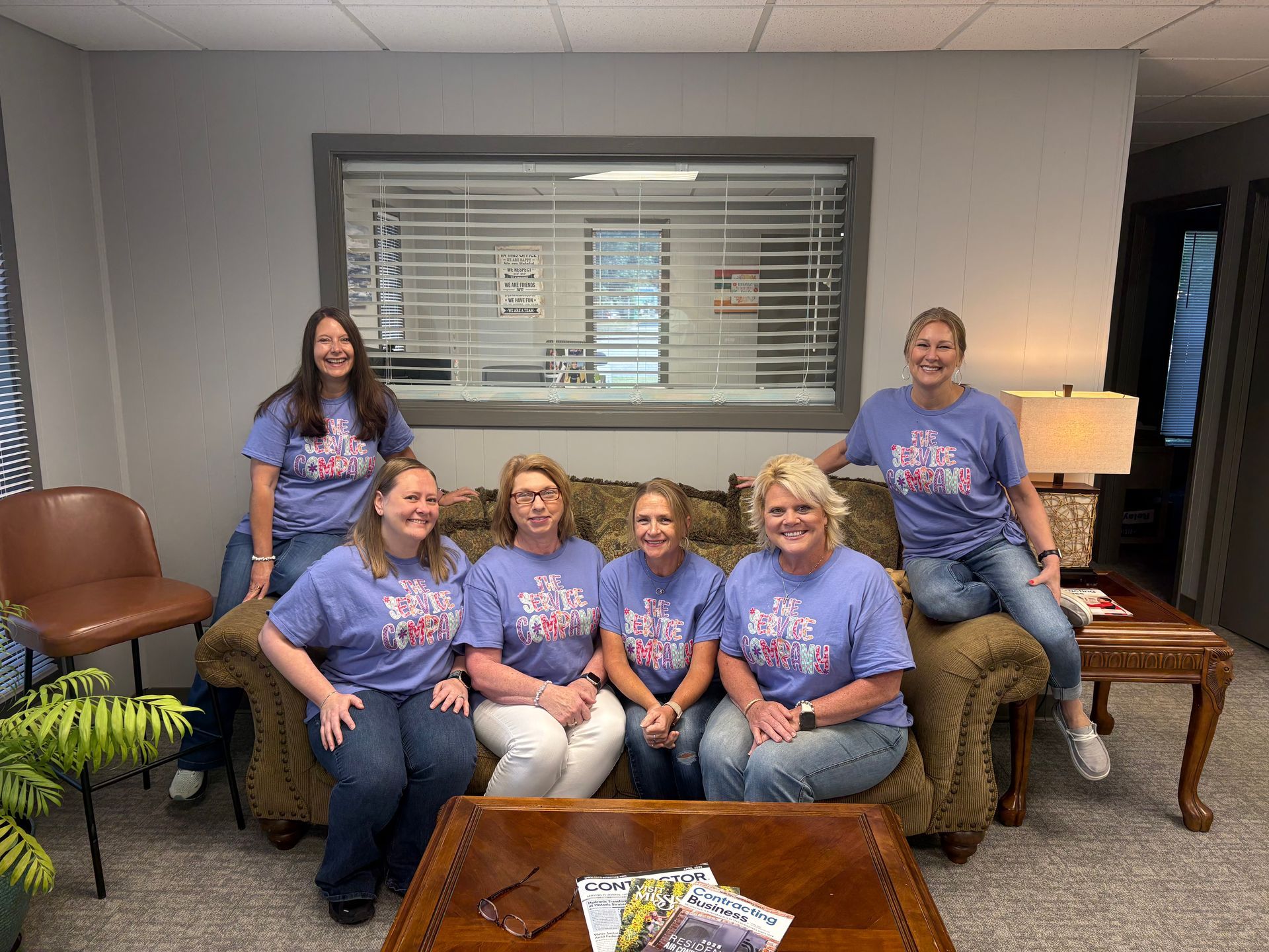 Six people in matching purple shirts seated in a lounge, smiling around a coffee table