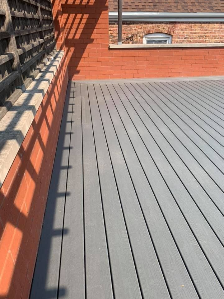 Empty rooftop deck with gray slatted flooring, red brick walls, and a railing casting shadows in sunlight
