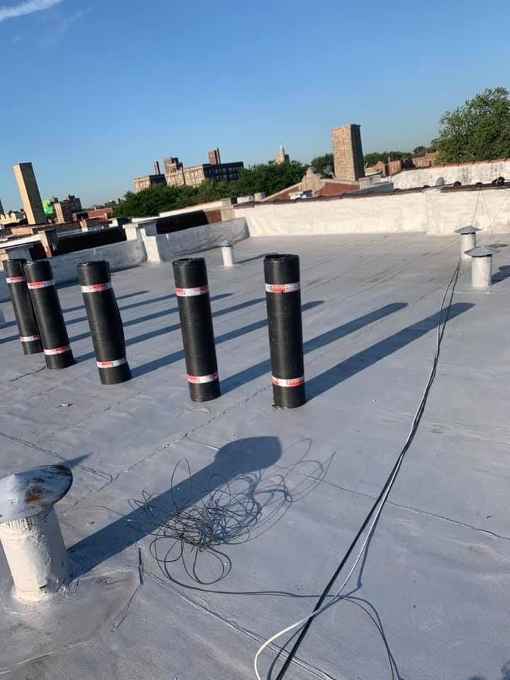 Rooftop with black vent pipes, white membrane roofing, and city buildings in the background