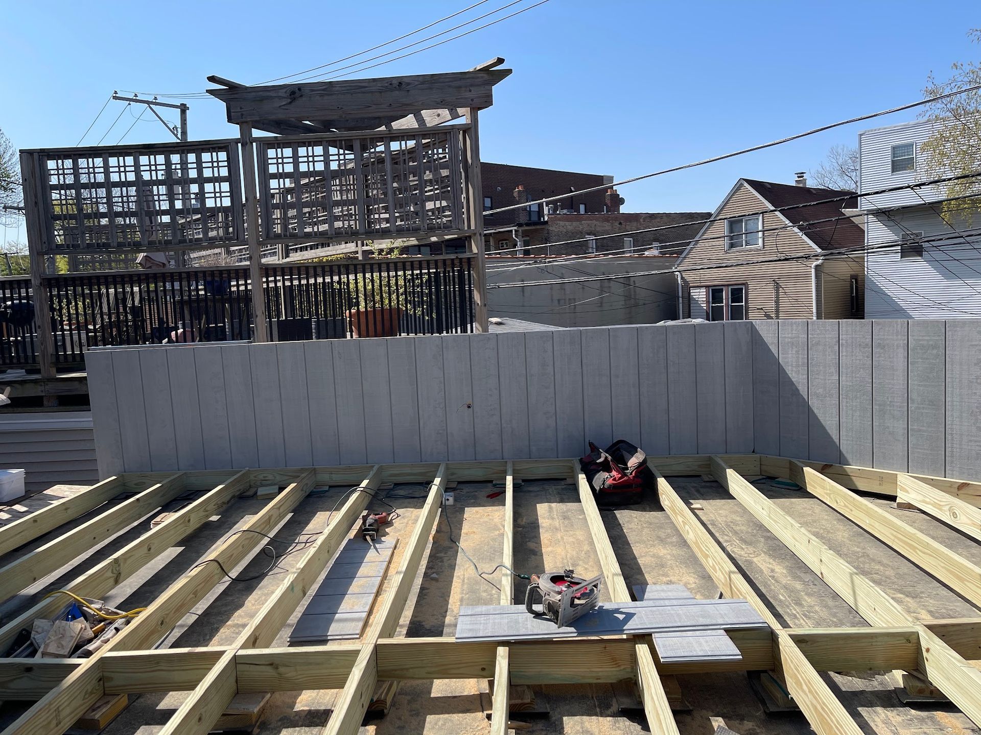 Partially built wooden deck framing in a backyard with a white fence and houses in the background