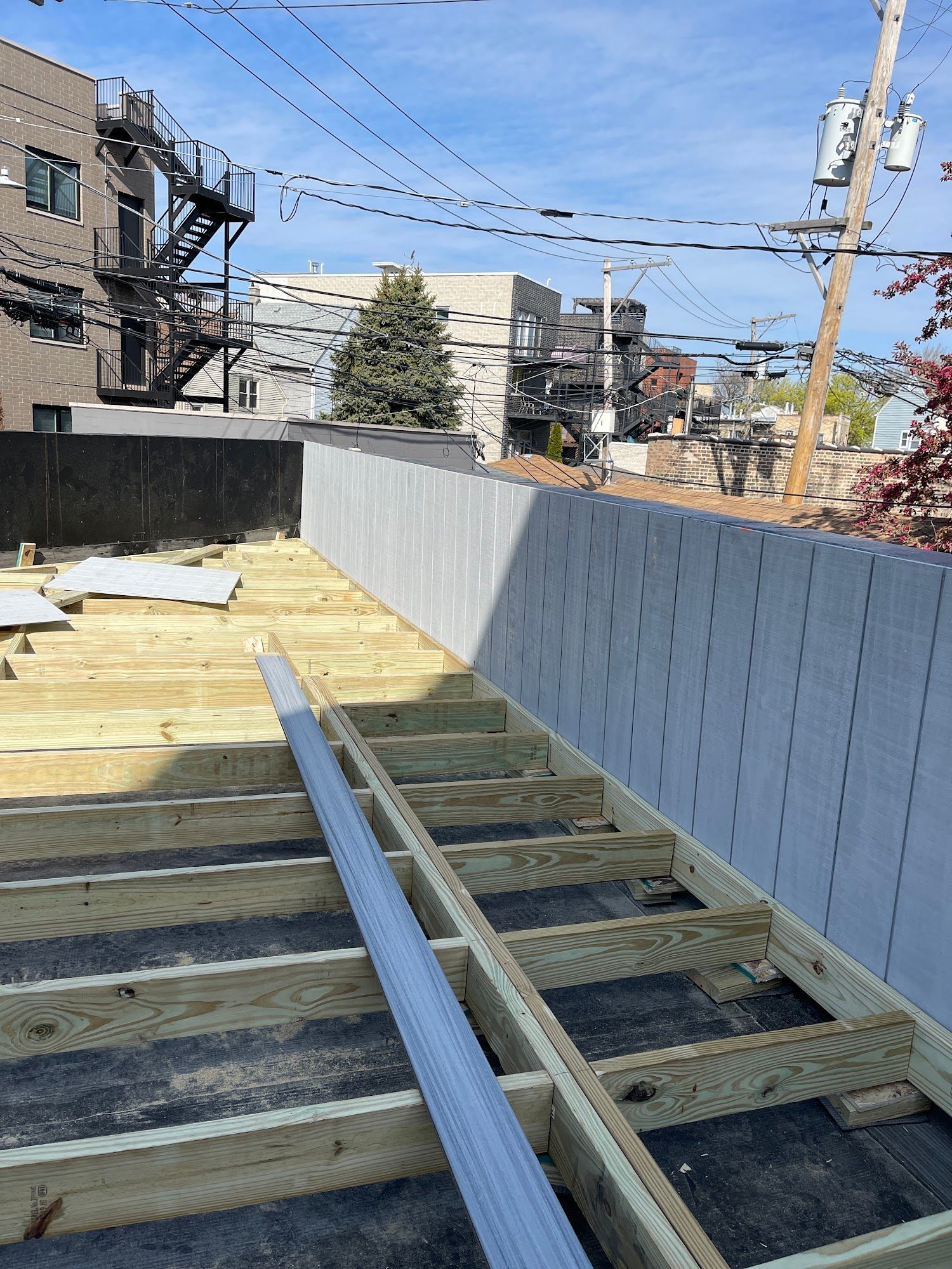 Partially built rooftop deck with wooden joists, metal beams, and city buildings in the background
