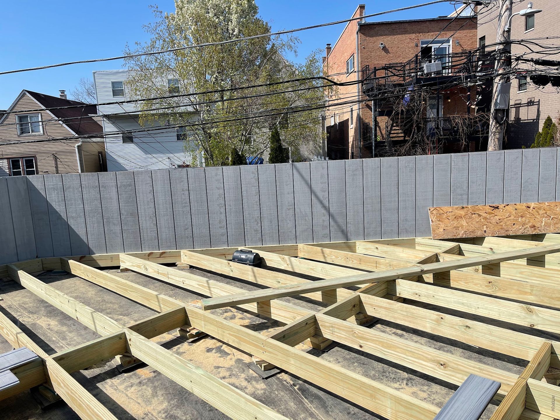 Wooden floor joists under construction in a backyard, with a gray fence and houses in the background