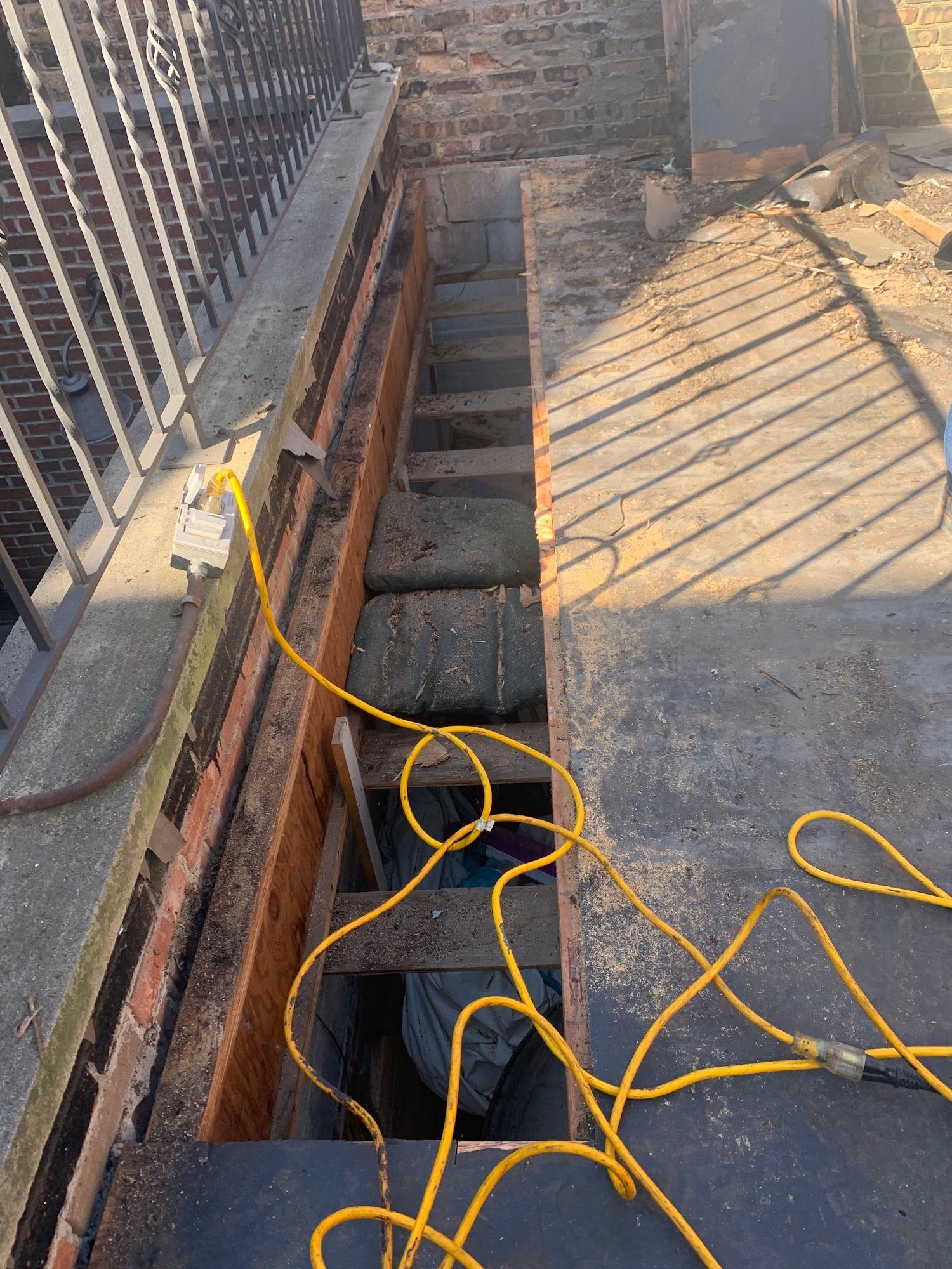 Open trench beside a brick wall with concrete blocks and a yellow extension cord on a rooftop.