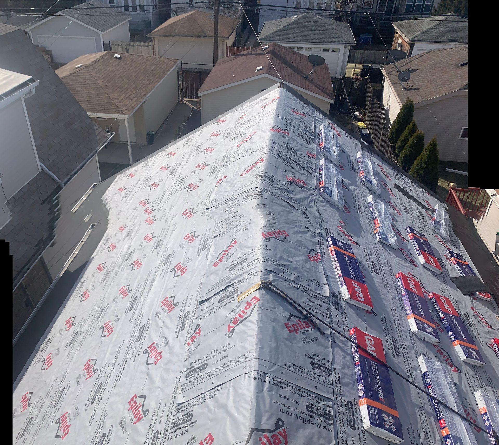 Roof under construction covered in white and blue waterproofing membrane, viewed from above between neighboring houses