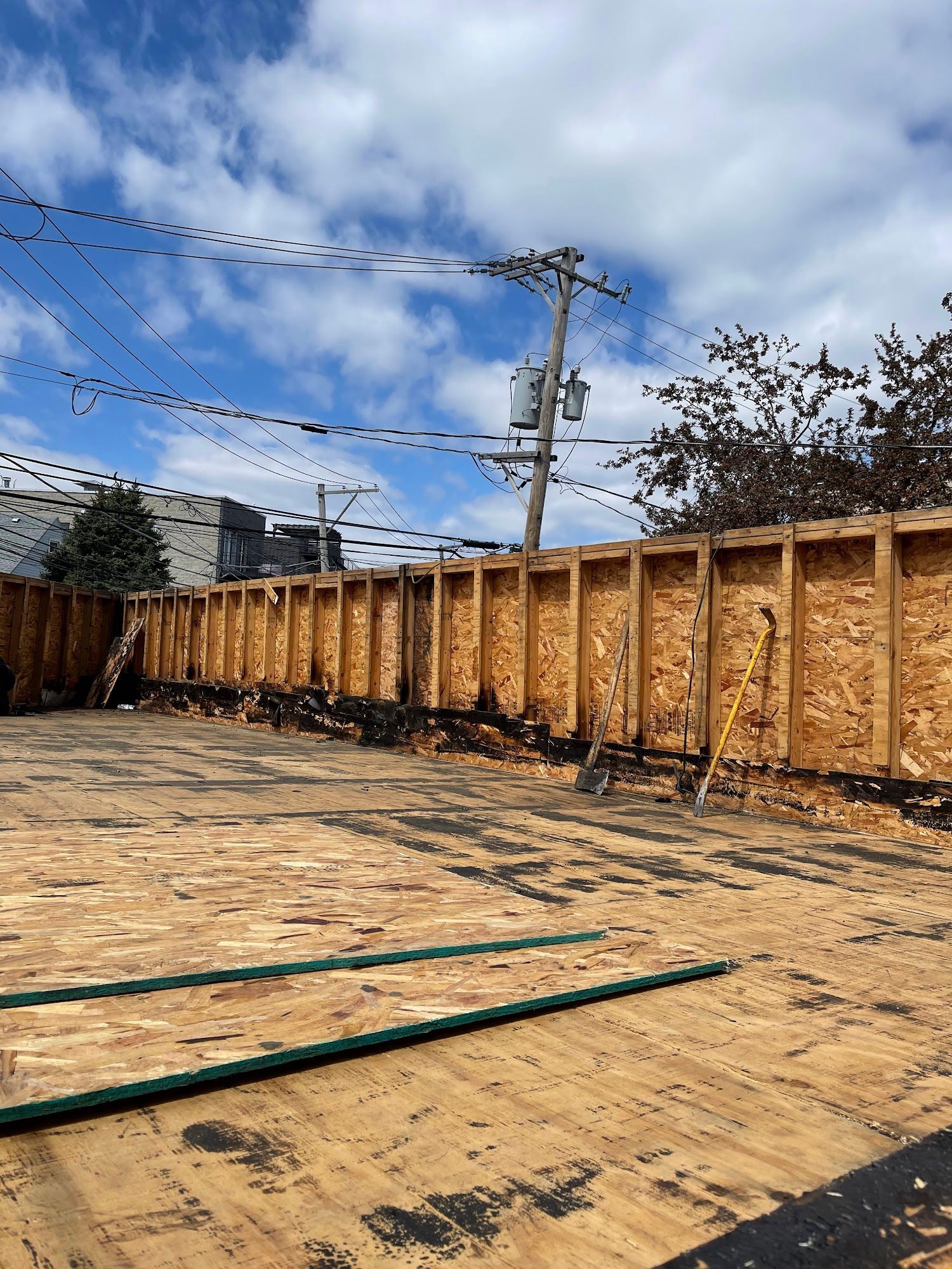Empty wooden construction site with plywood floor, fence, utility pole, and cloudy sky