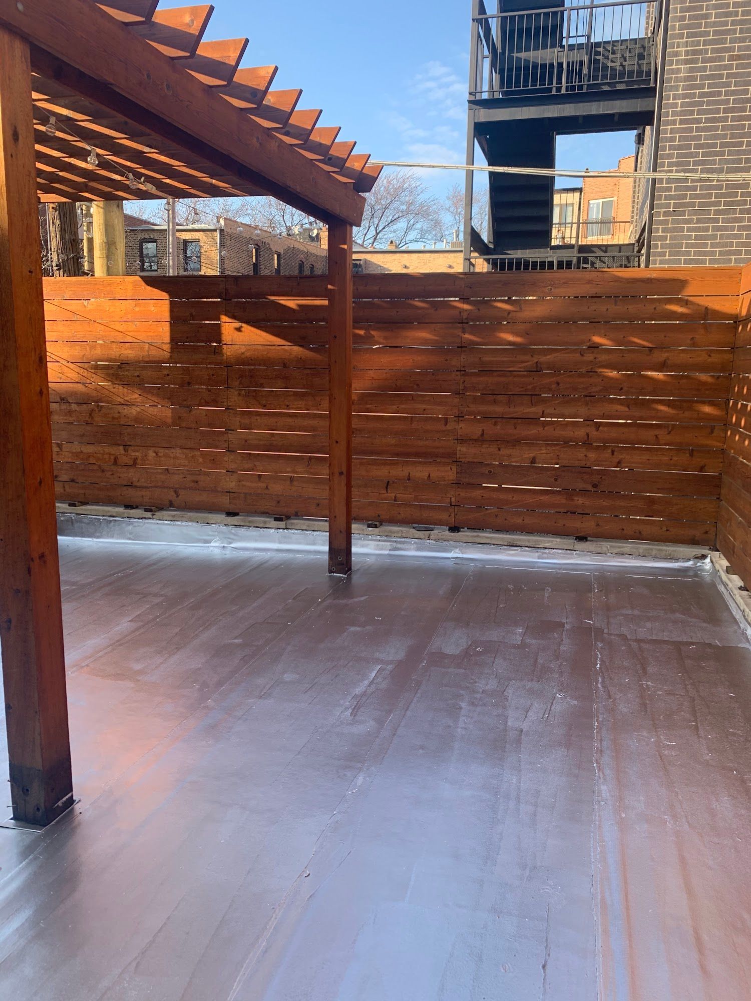 Covered outdoor patio with wood pergola, privacy fence, and freshly coated concrete floor.