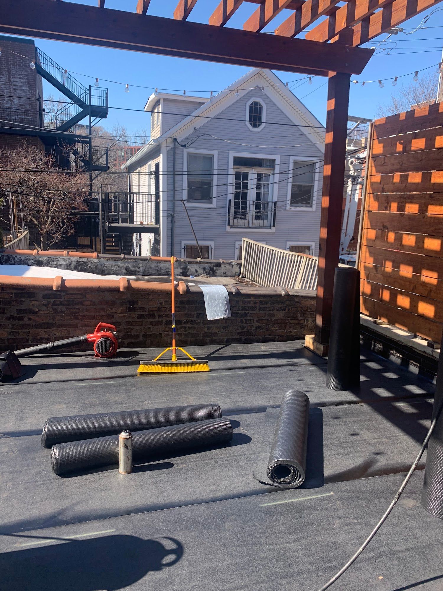 Patio under wooden pergola with construction materials, tools, and a house in the background