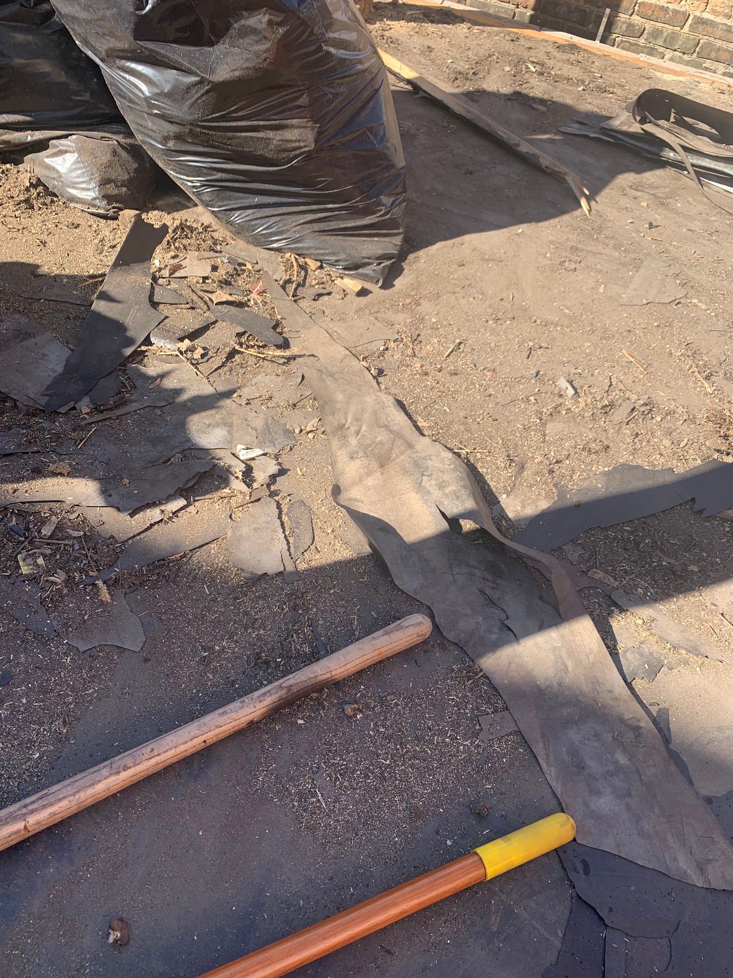 Broken pavement beside black trash bags and a copper pipe on dirt ground.