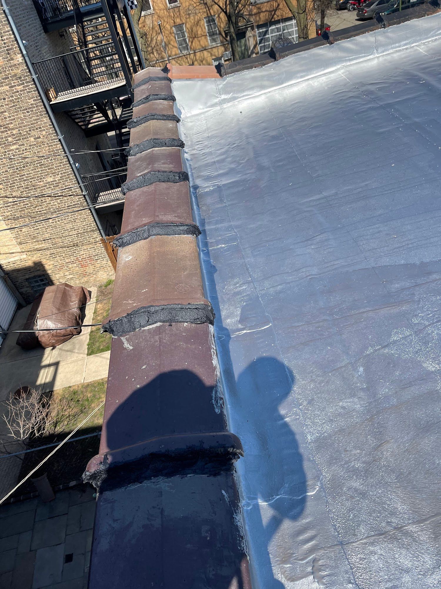 Rooftop with rolled roofing and brick edge, viewed along the roofline on a sunny day.