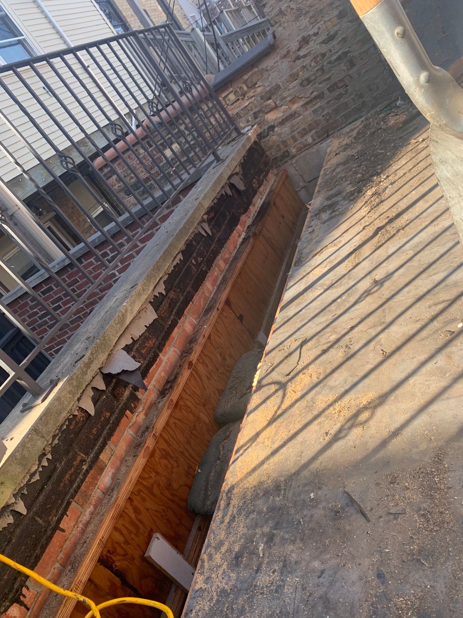 Open utility trench beside a sidewalk, with exposed brick, pipes, and metal railing.