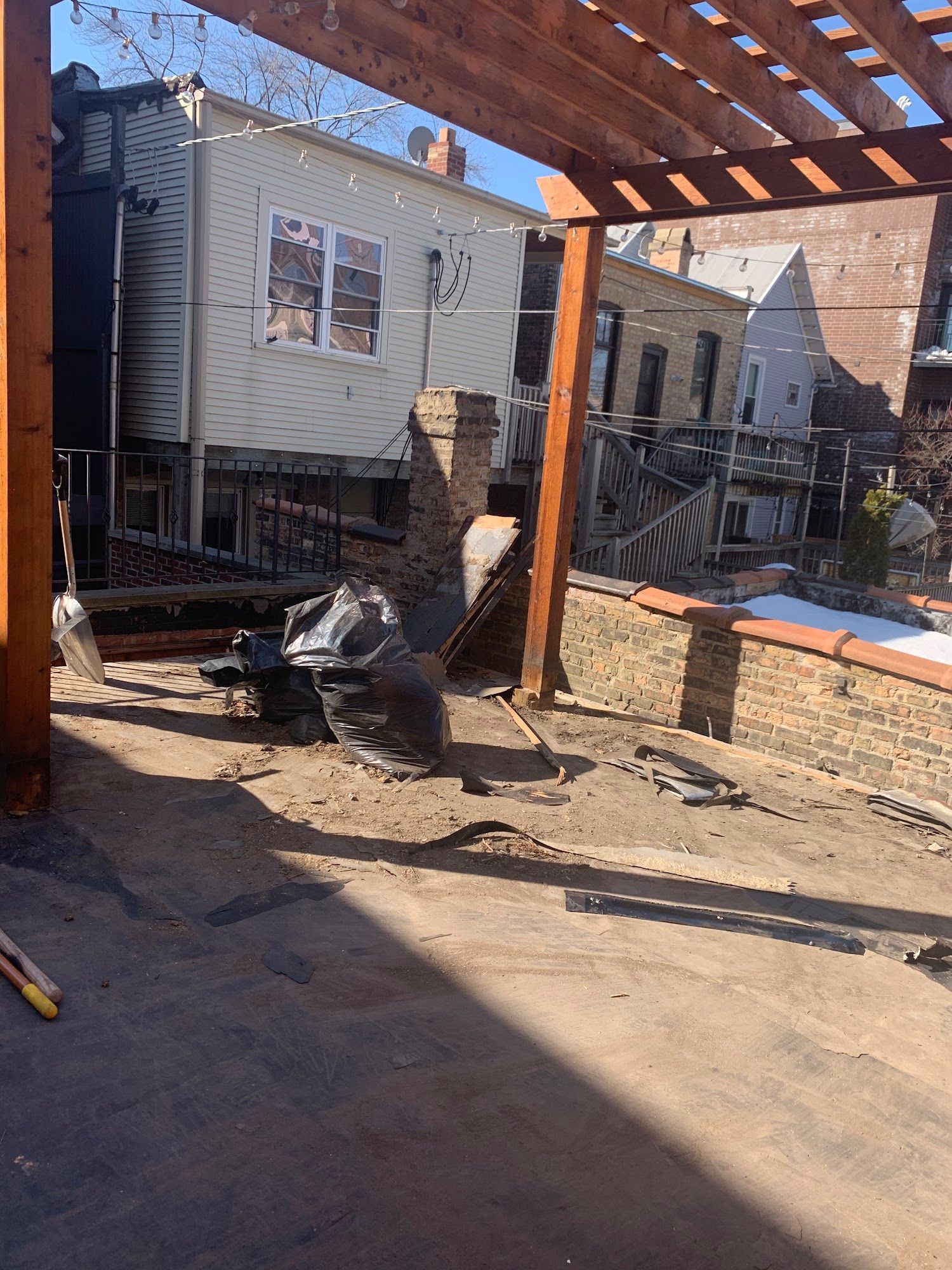 Backyard patio with wooden pergola, house siding, and outdoor furniture in sunlight