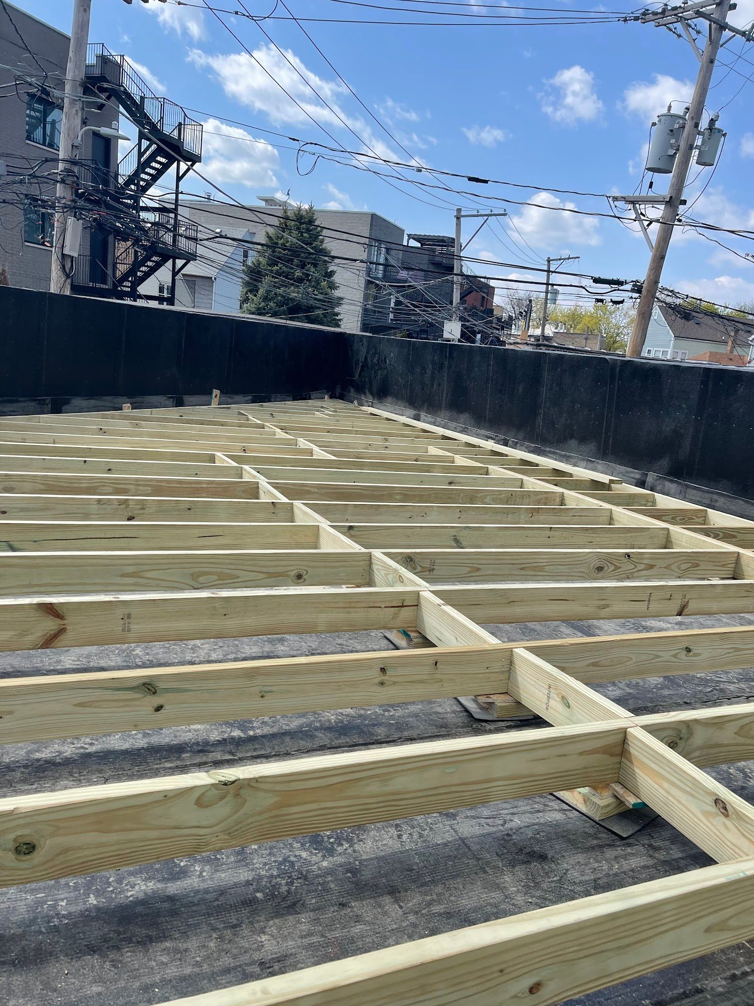 Wooden floor framing under construction in an outdoor lot with utility poles and overhead wires.