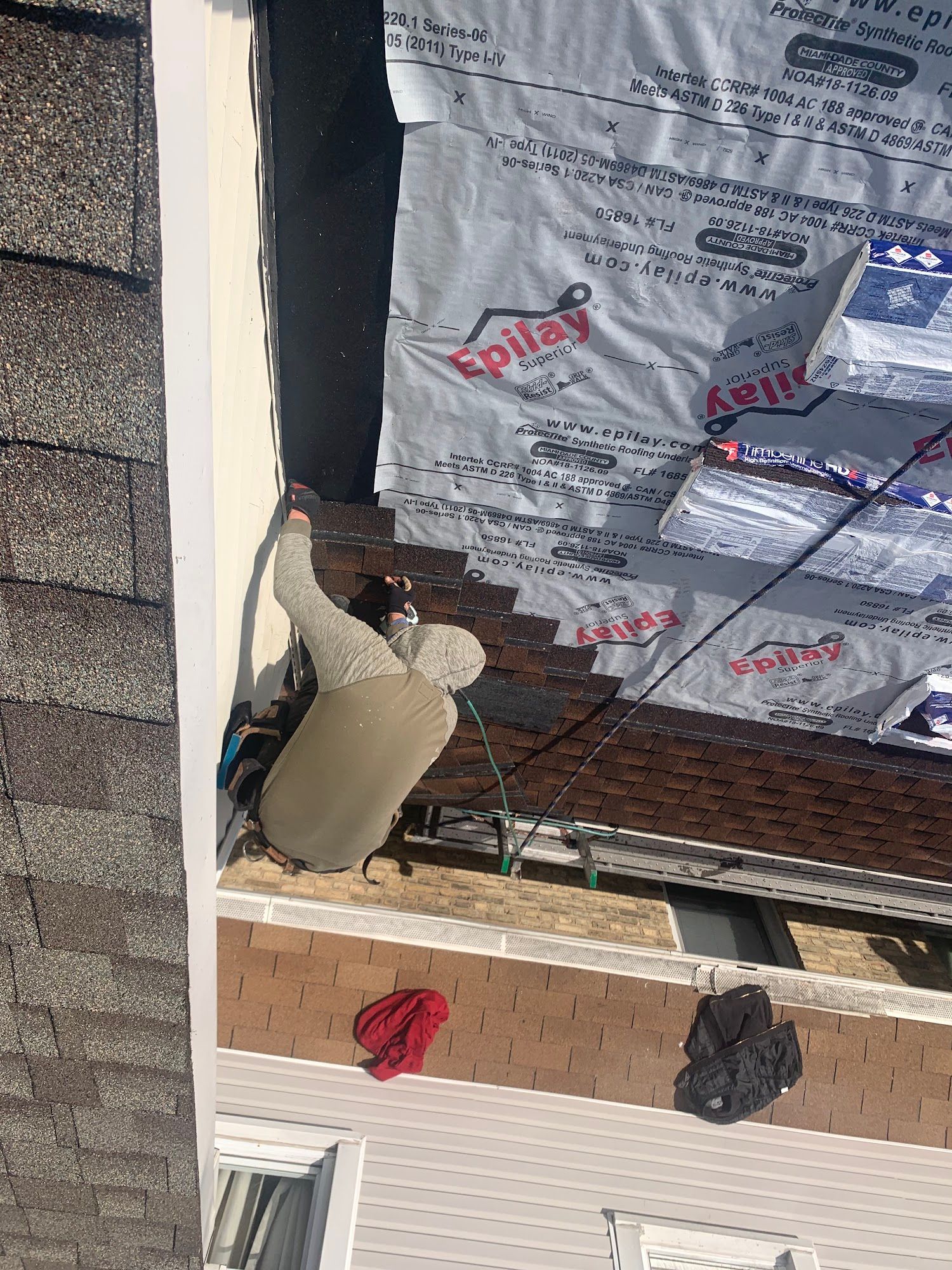 Worker installing insulation on a building roof beside brick chimney and shingles