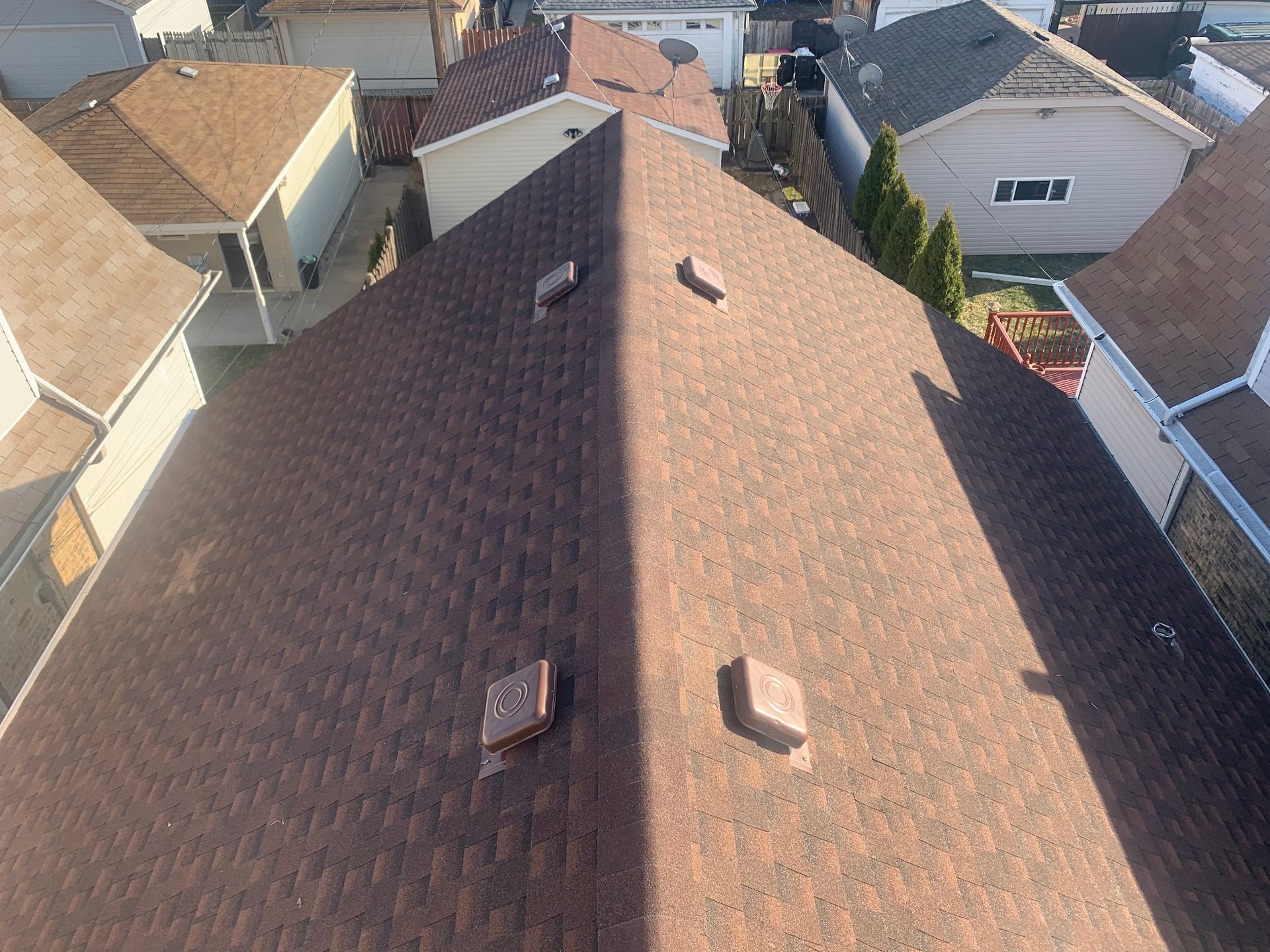 Aerial view of a brown shingled house roof with skylights, surrounded by neighboring homes.