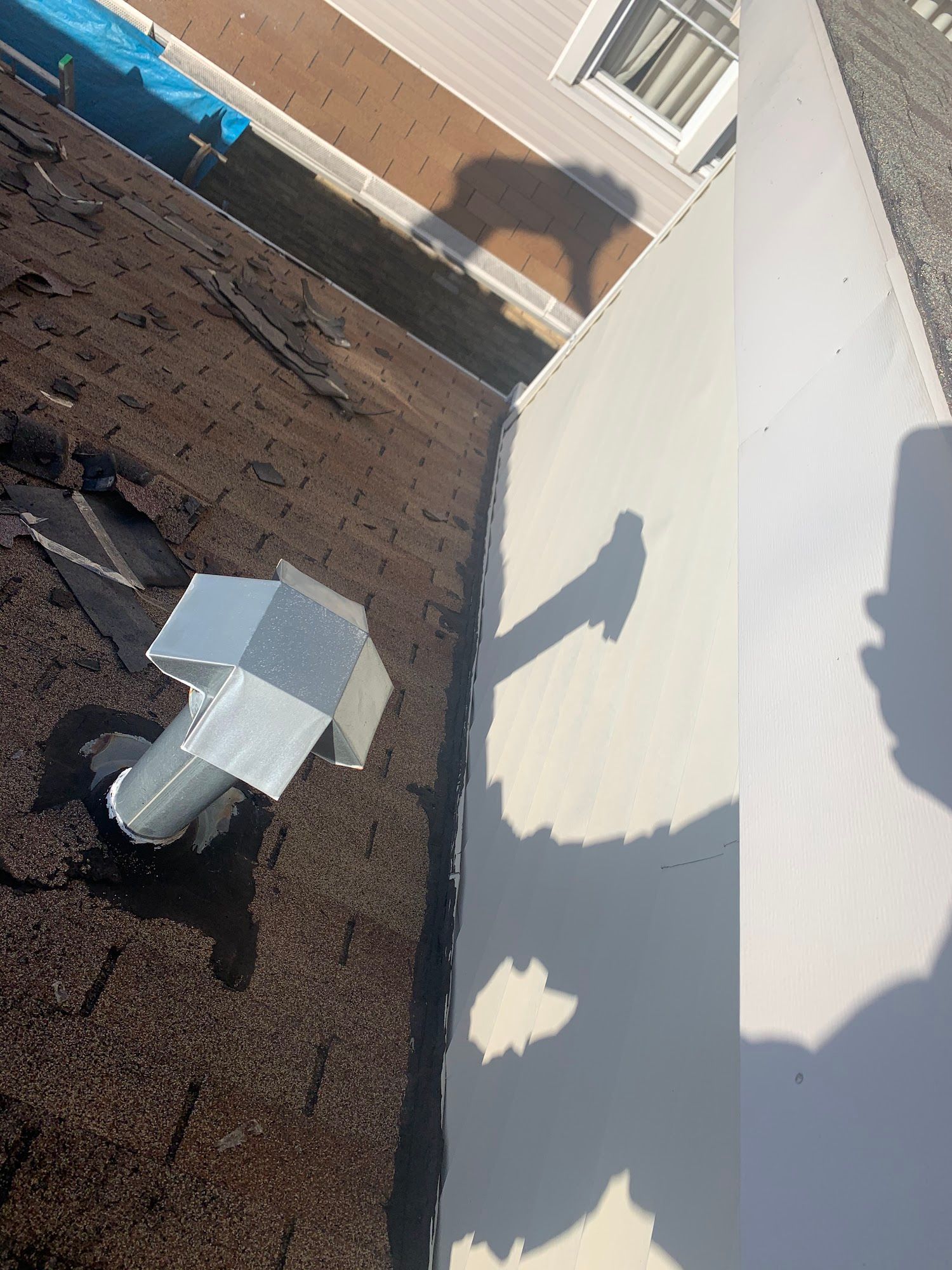 Rooftop with HVAC vent, brick wall, and bright sun casting shadows on a white surface