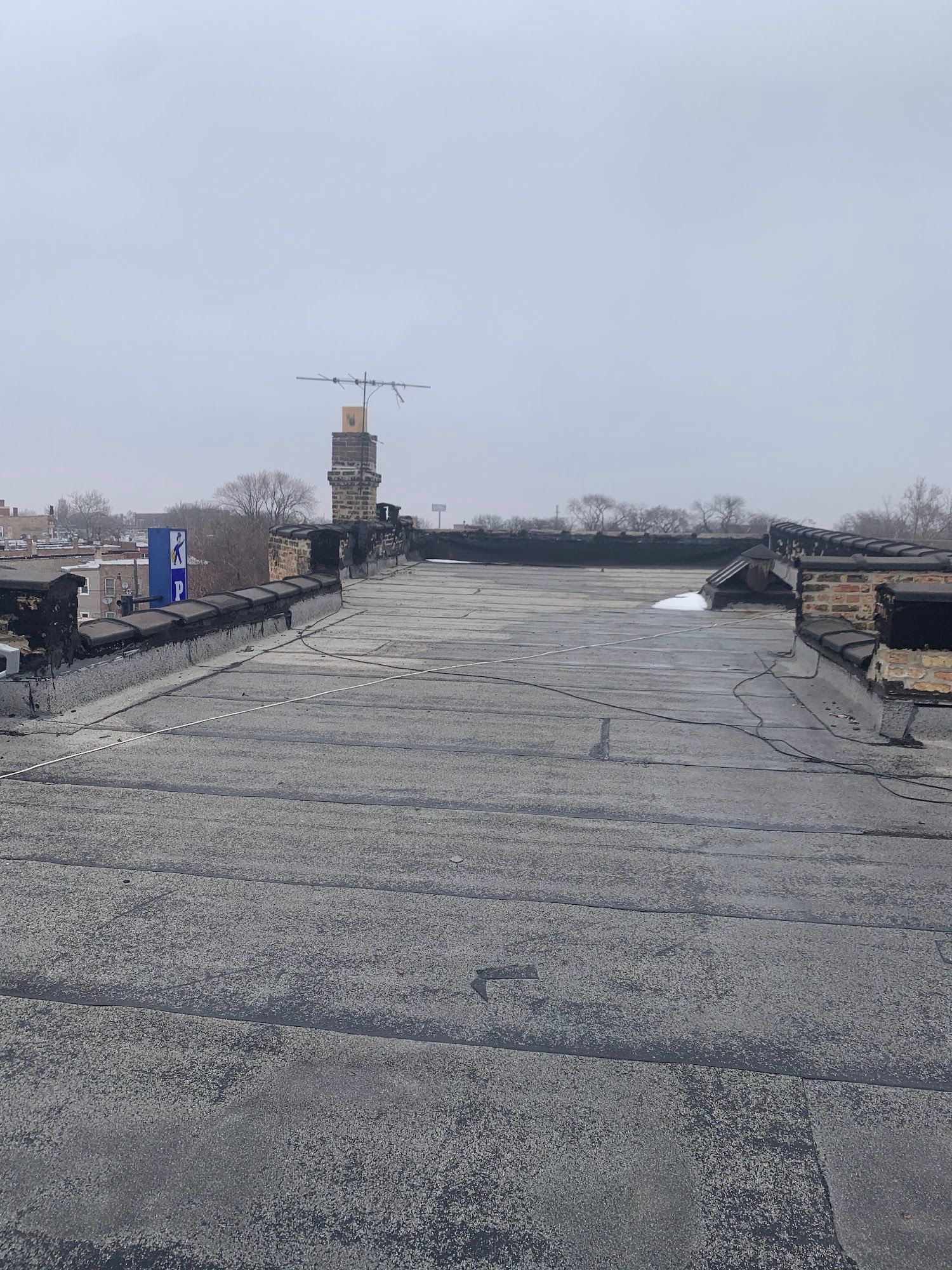 Rooftop with gray gravel surface under an overcast sky, with a distant construction crane and equipment.