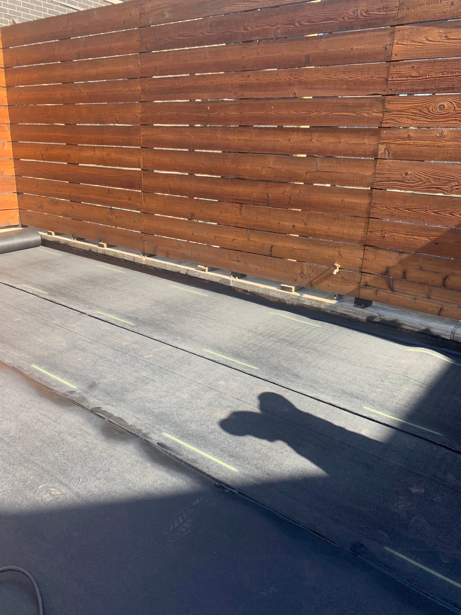 Sunlit wooden fence beside a concrete sidewalk with a person’s shadow in the foreground