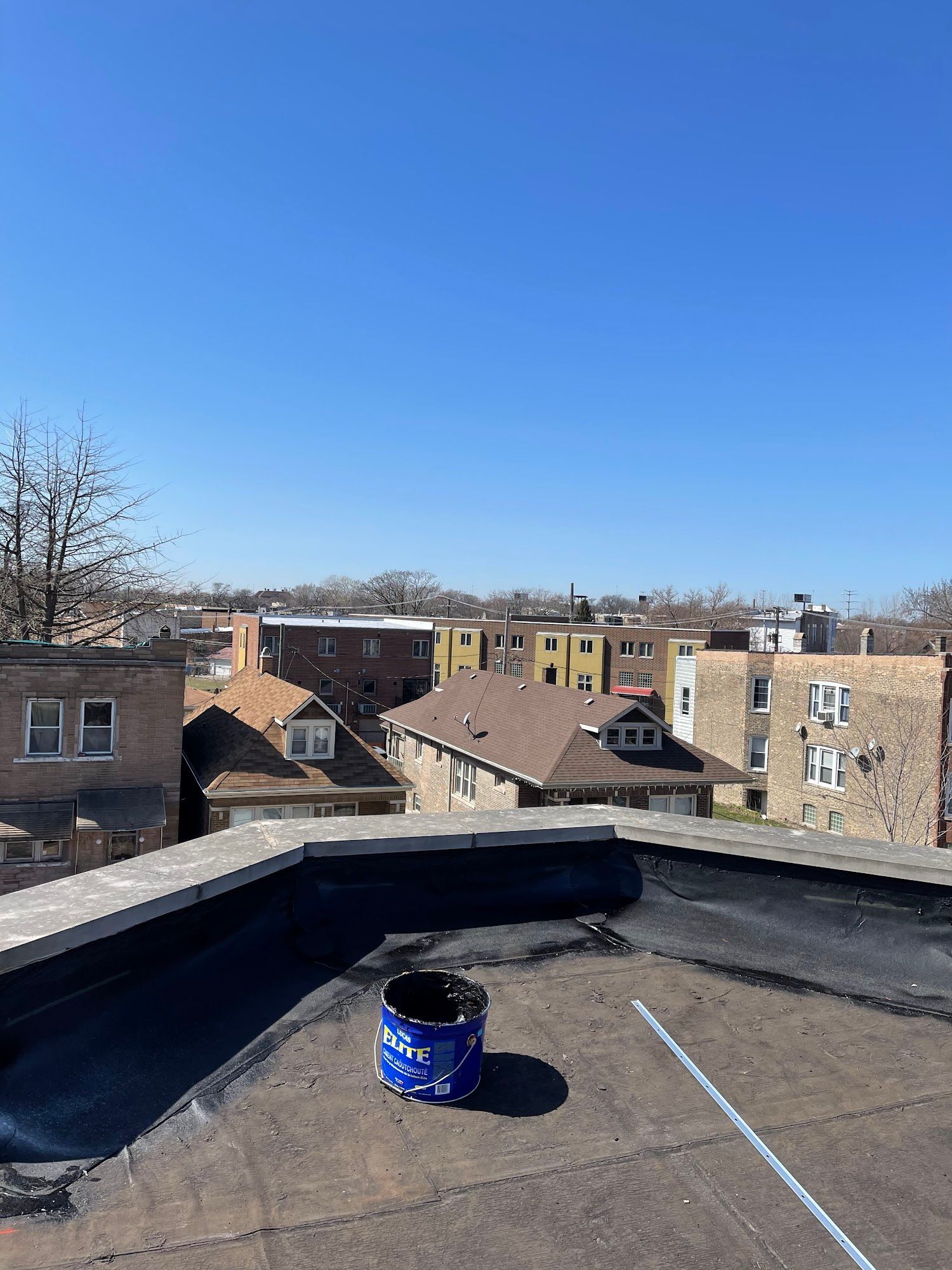 Rooftop view with a blue bucket in the foreground, surrounded by buildings under a clear blue sky.
