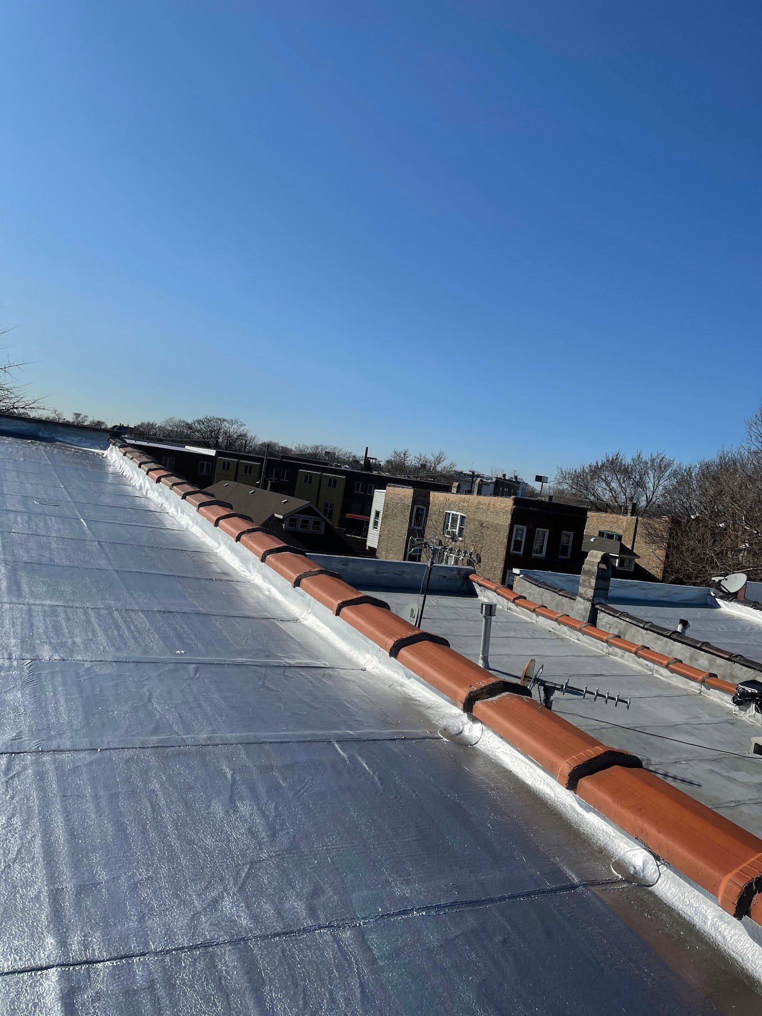 Rooftop with silver membrane and red vent pipe under a clear blue sky