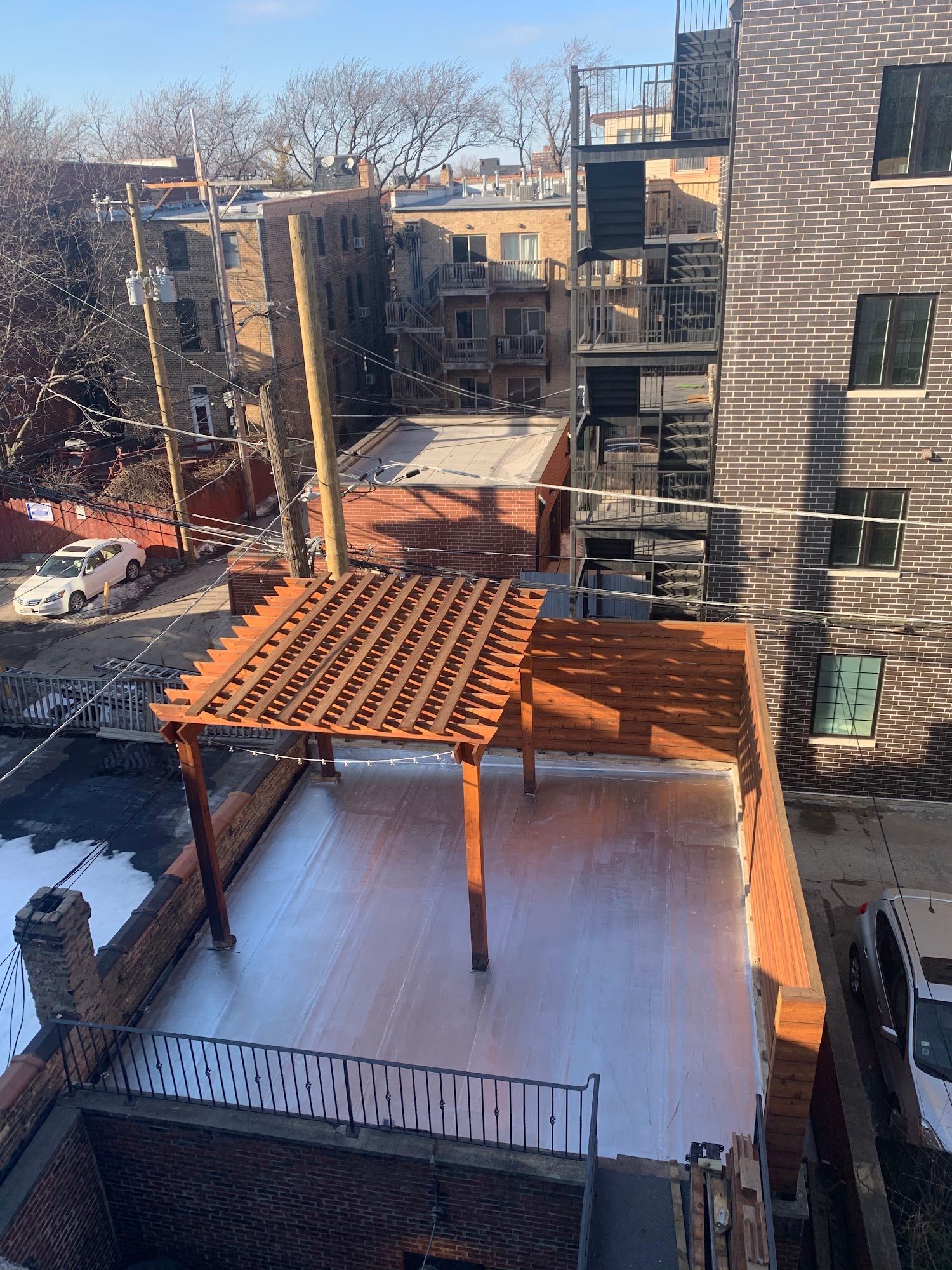 Snowy rooftop courtyard between apartment buildings with a wooden pergola and black metal railing